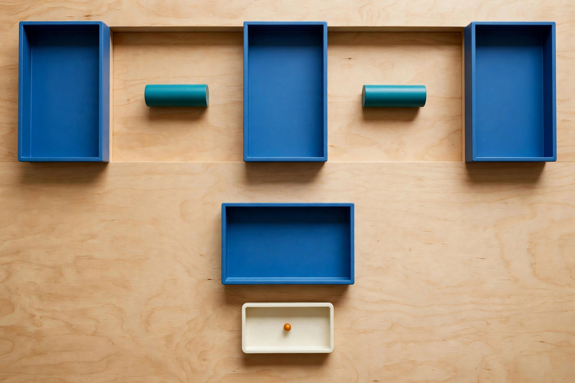 Three blue trays and two teal cylinders are arranged on a wooden surface, with a fourth ivory tray containing an orange bead below.