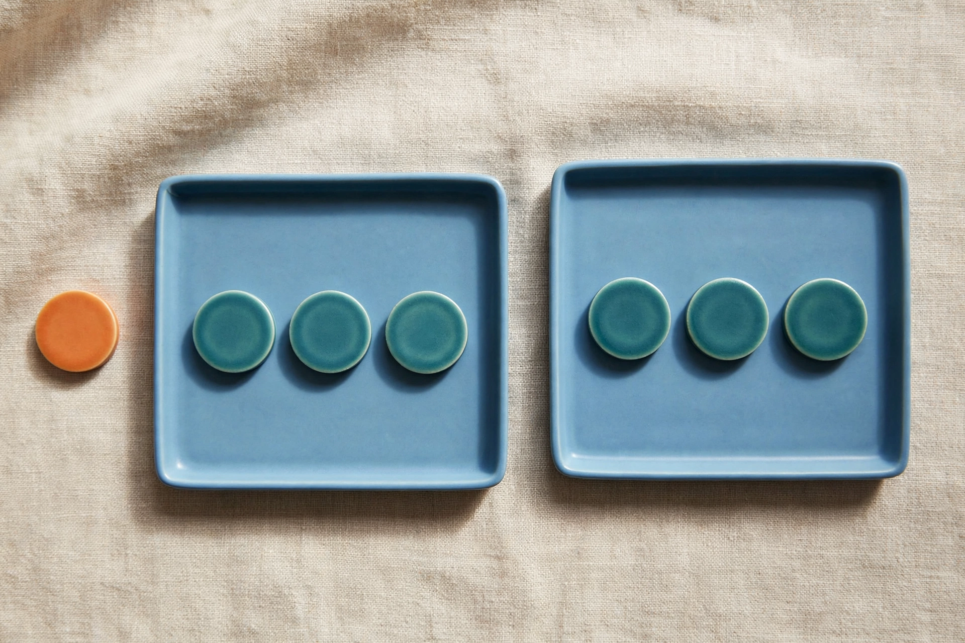 Two blue trays hold teal tokens, with an orange token beside one tray on a textured surface.