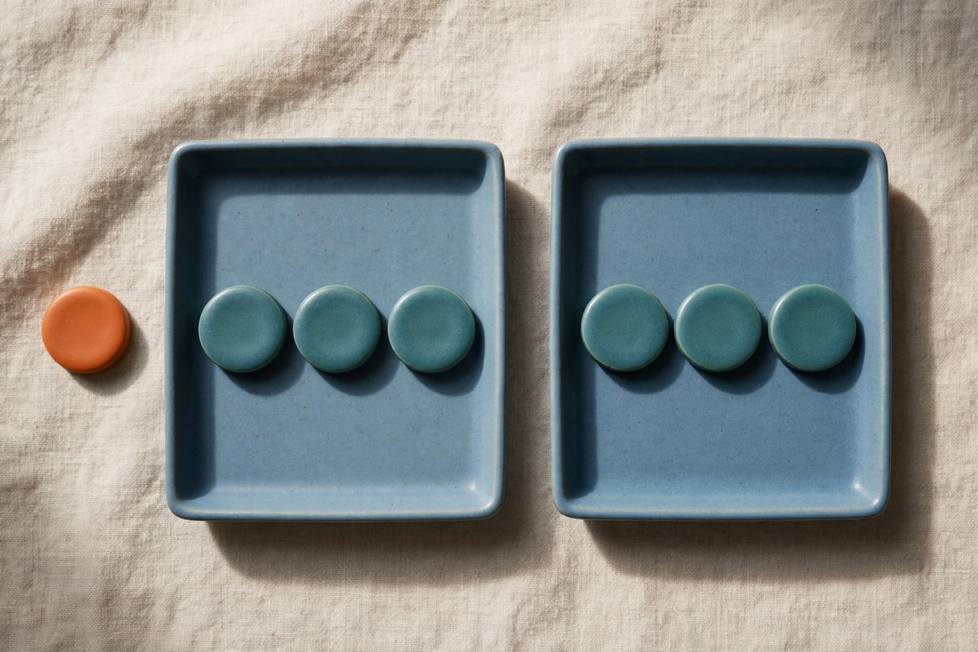 Two blue trays each hold three teal tokens, with one orange token placed beside the left tray on a textured surface.
