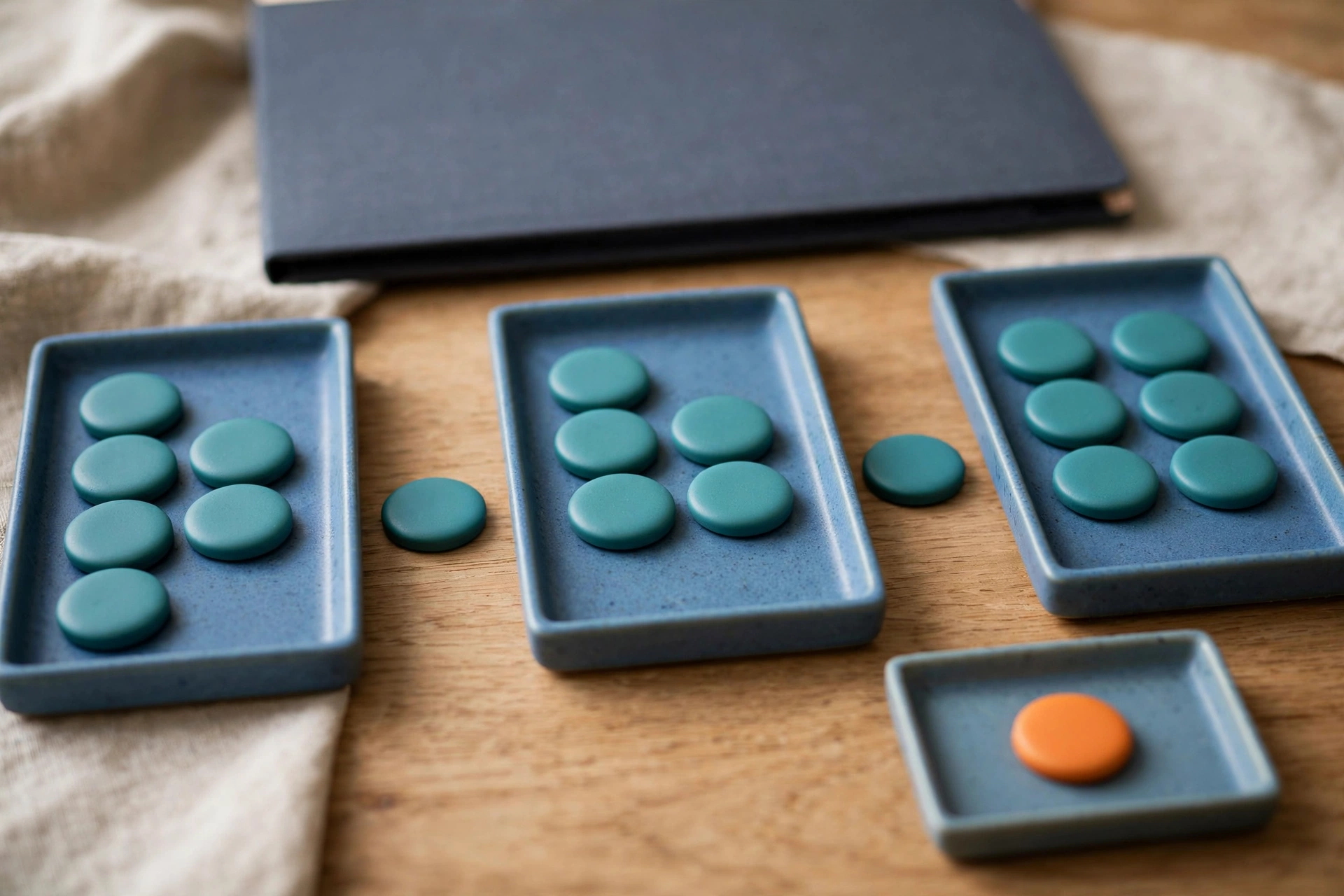 Three blue trays with teal tokens in a sequence, a separate tray with an orange token, and a closed folder behind.