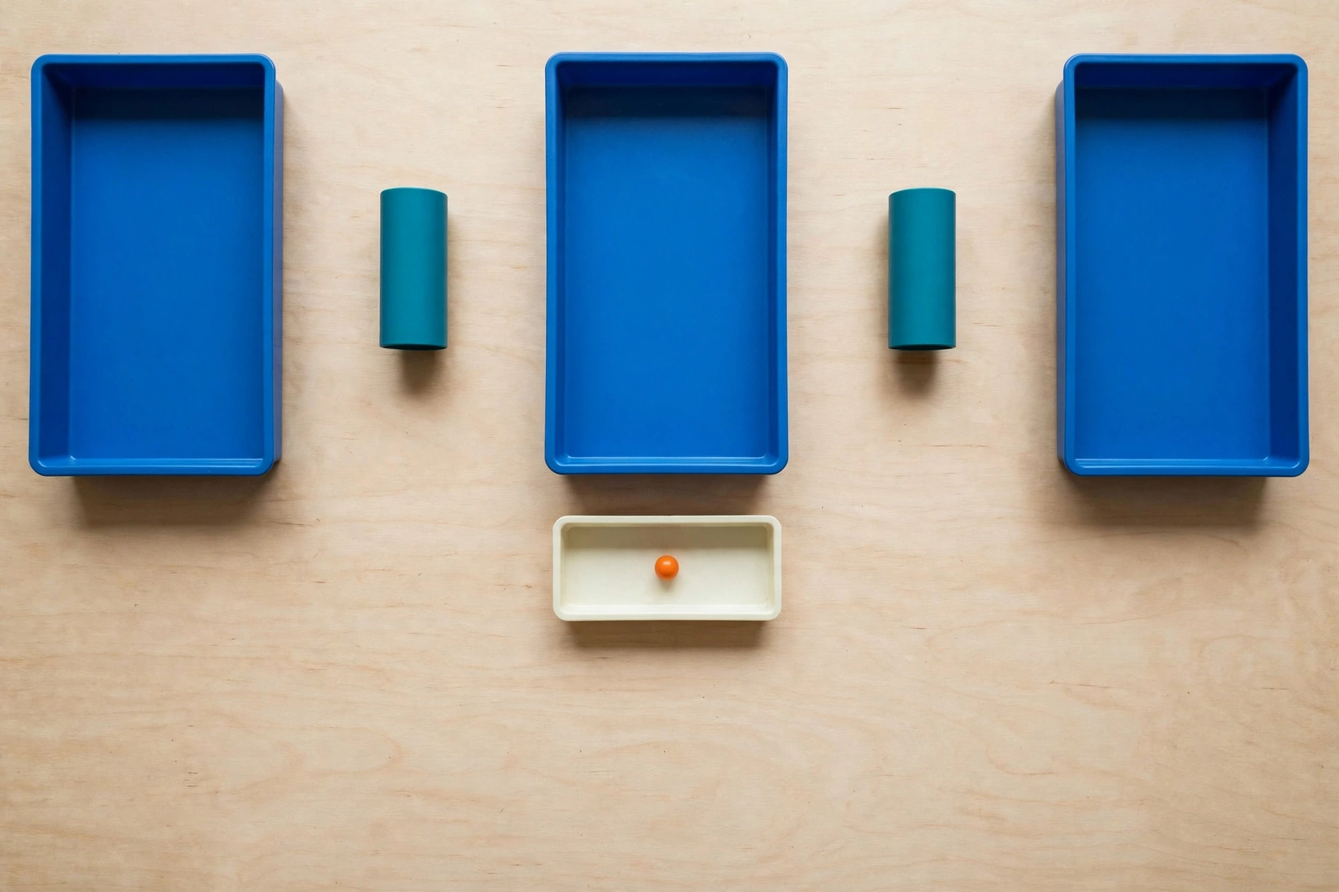 Three blue trays and two teal cylinders are arranged on a wooden surface, with one orange bead in a lower ivory tray.