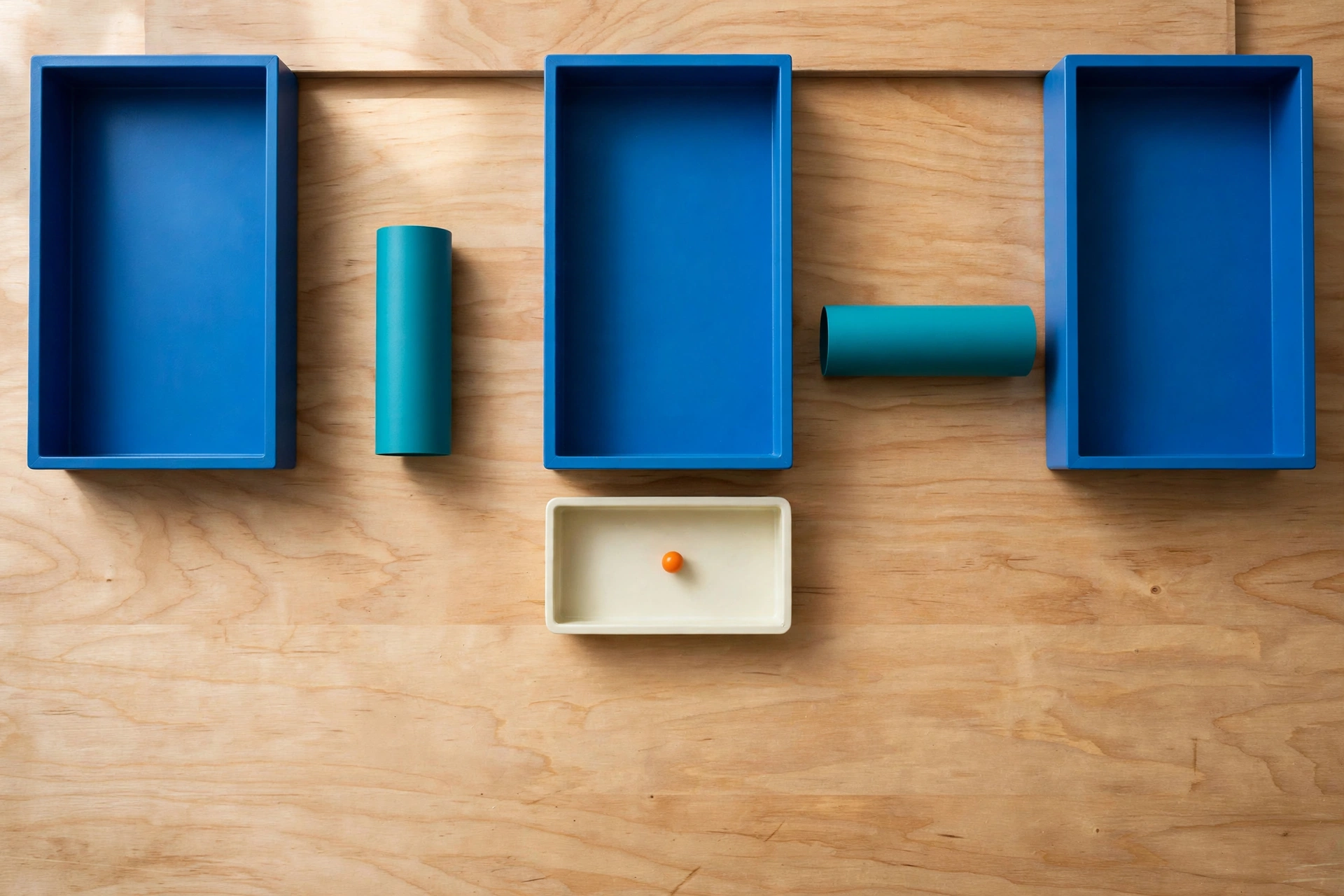 Three blue rectangular trays are arranged in a row on a wooden surface, with teal cylinders placed in the gaps between them.