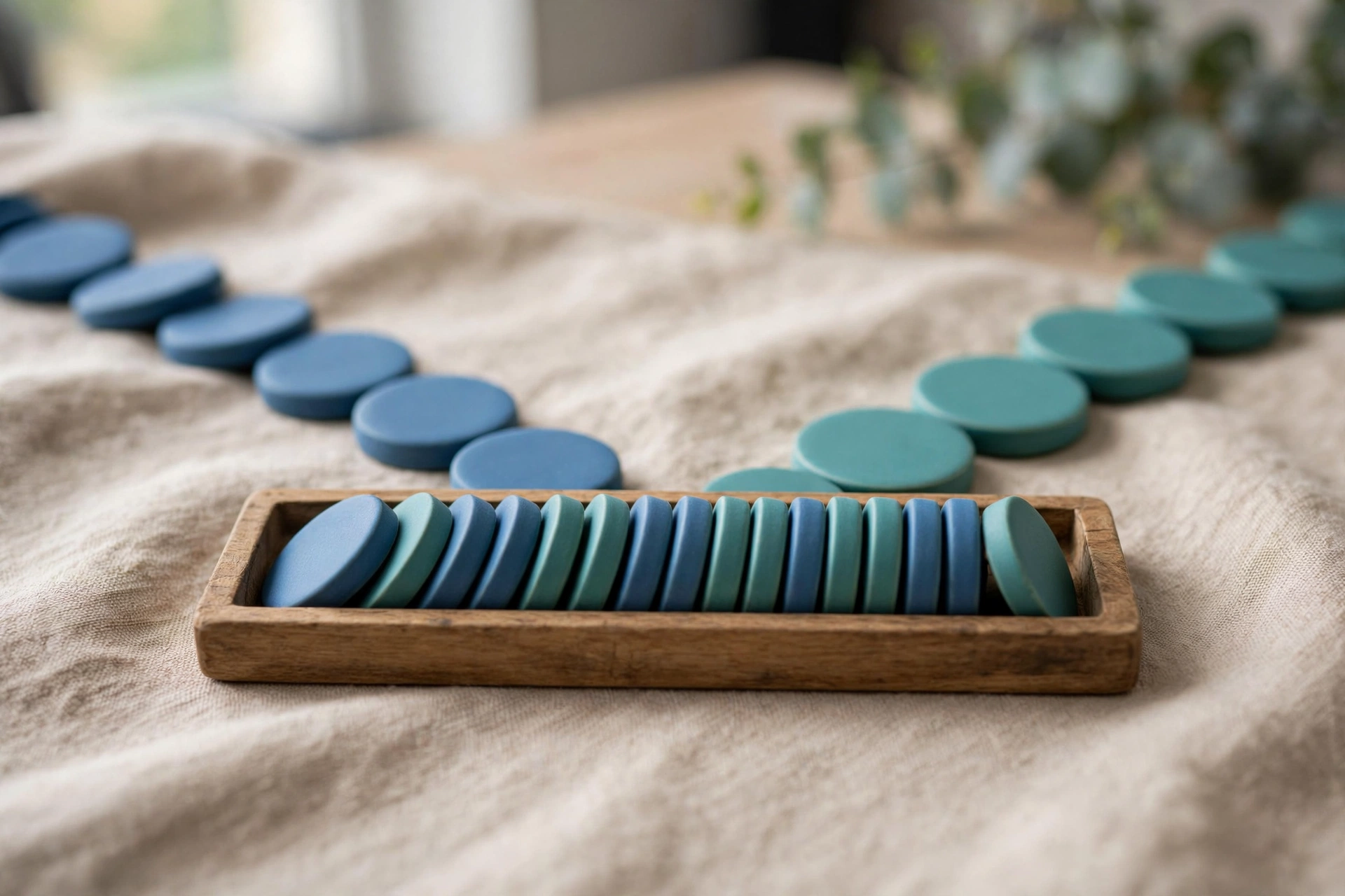 Two streams of blue and teal tokens converge into a single row in a wooden tray on a textured surface.