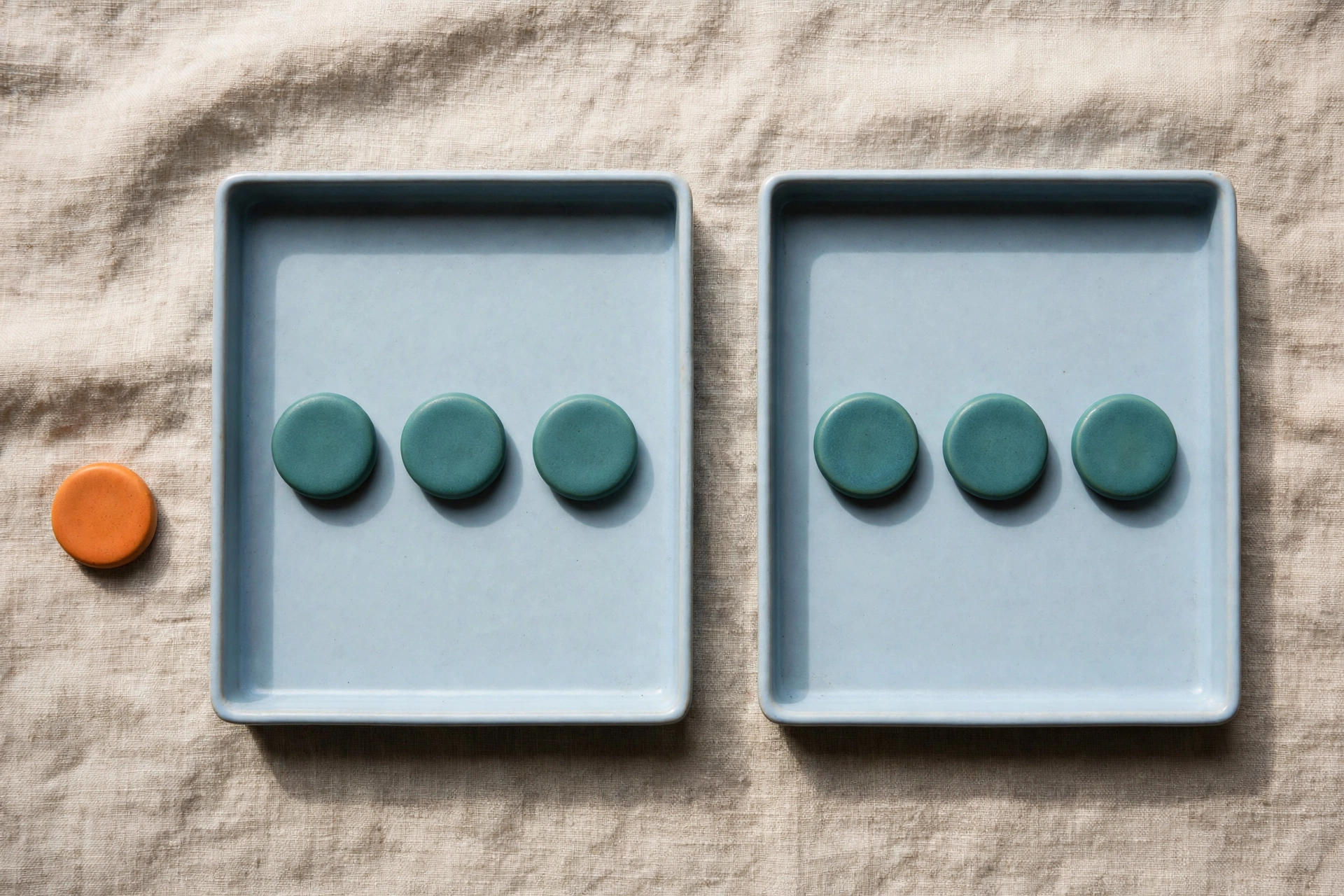 Two blue trays hold teal tokens, with an orange token placed beside the left tray on a textured surface.
