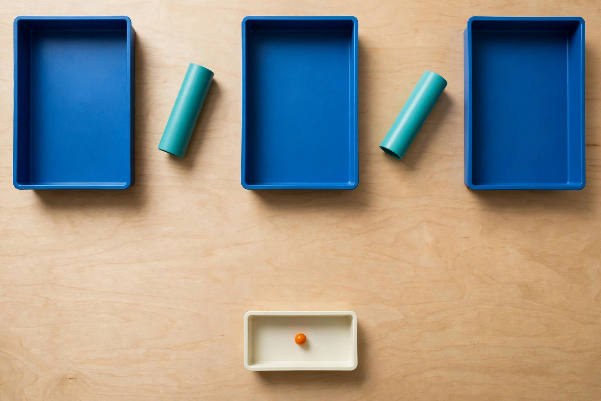 Three blue rectangular trays are arranged in a row with two teal cylinders in the gaps between them, and an orange bead in a lower ivory tray.