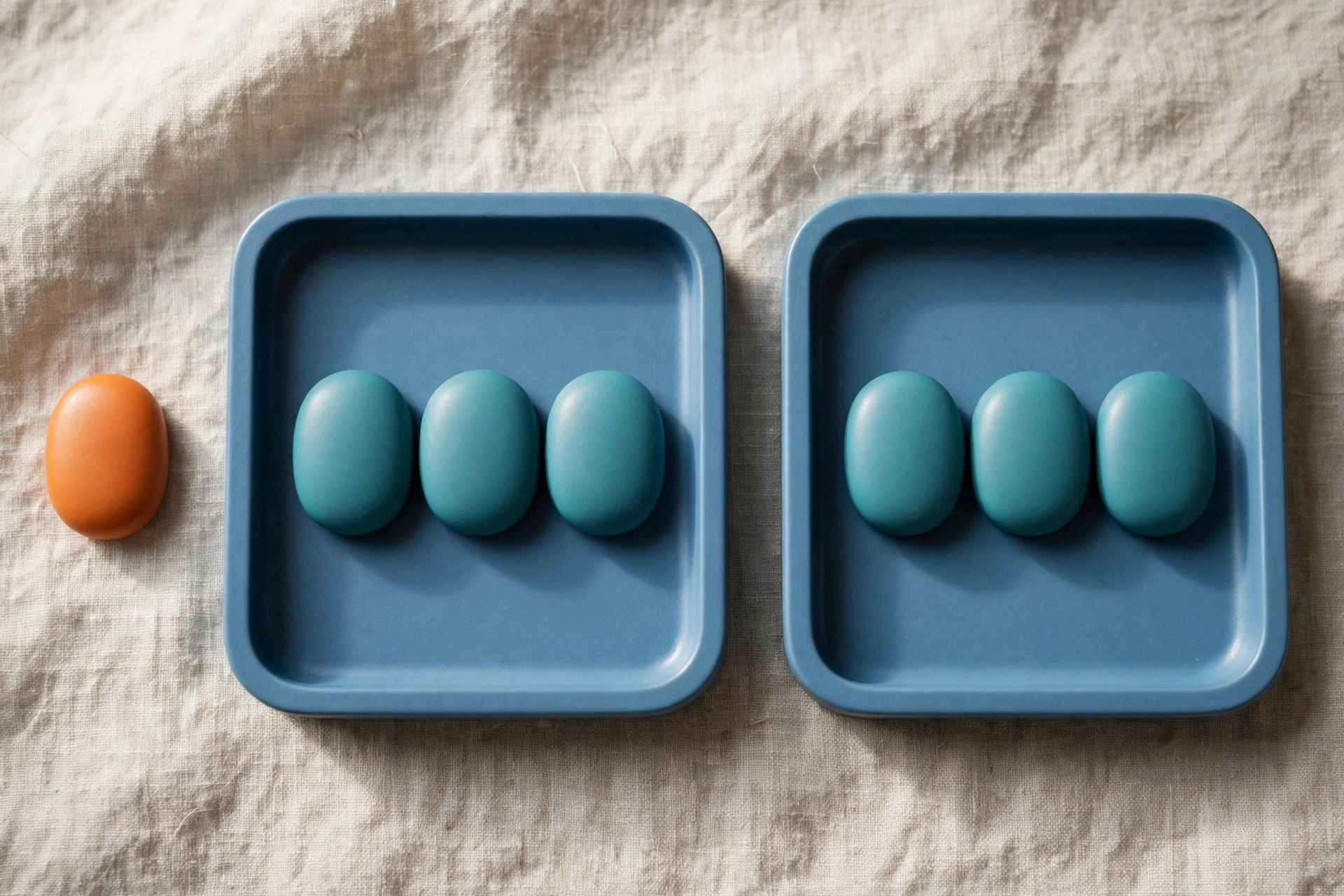Two blue trays hold teal tokens, with an orange token placed separately beside one tray on a textured surface.