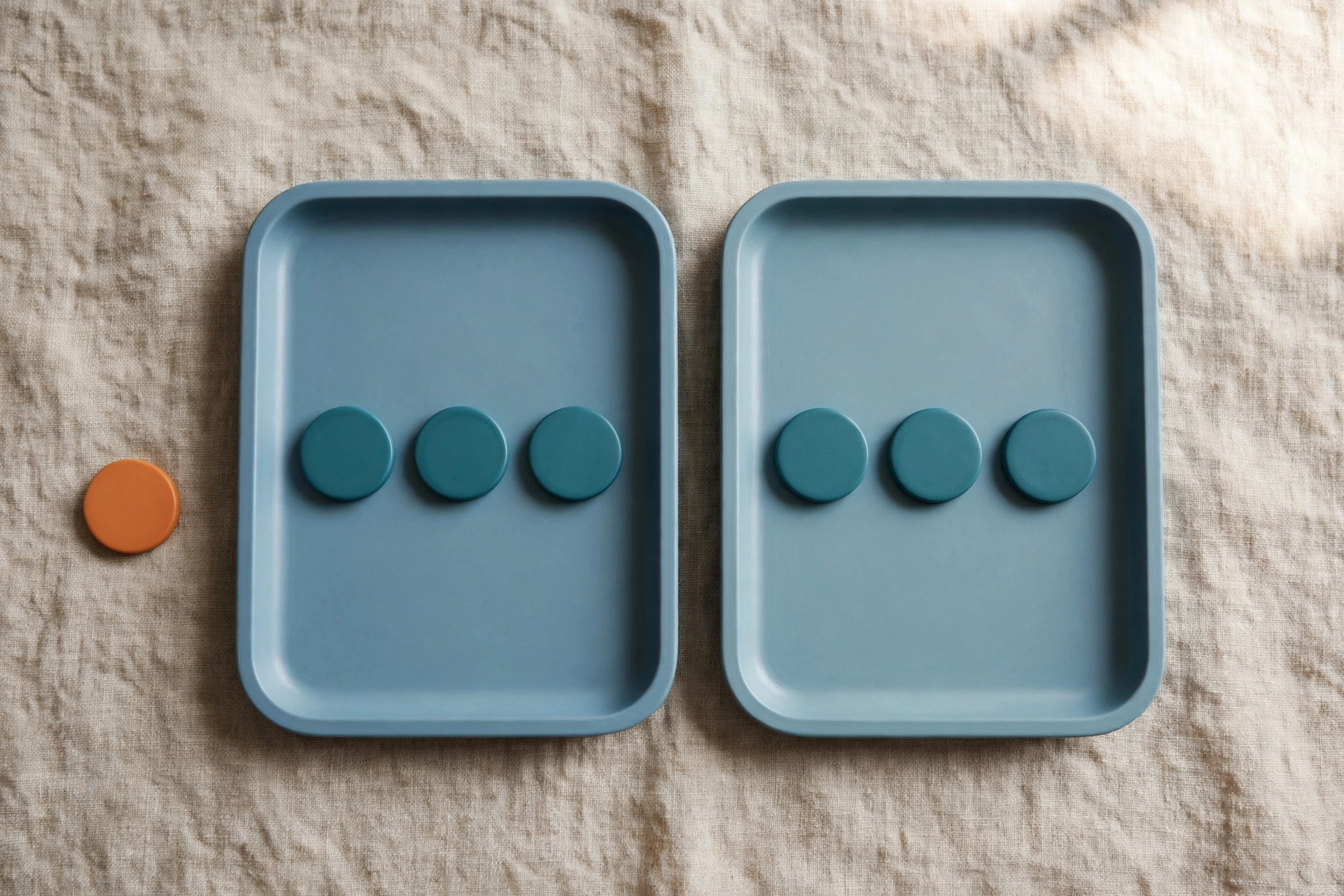 Two blue trays with teal tokens sit side-by-side on a textured surface, with an orange token placed beside one tray.