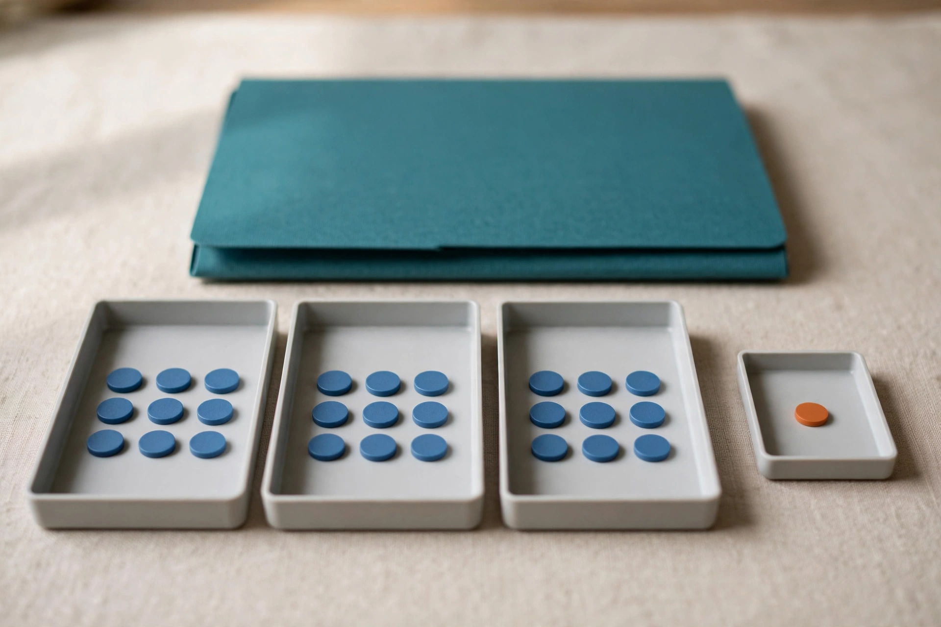 Three trays hold blue tokens, and a fourth tray holds a single orange token, with a teal folder behind them.