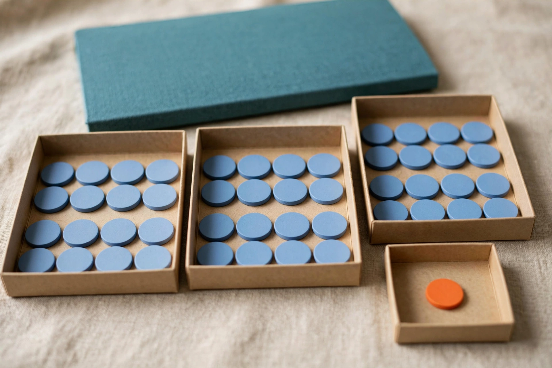 Blue tokens are distributed in three trays, with one orange token in a separate small tray, and a teal box behind.