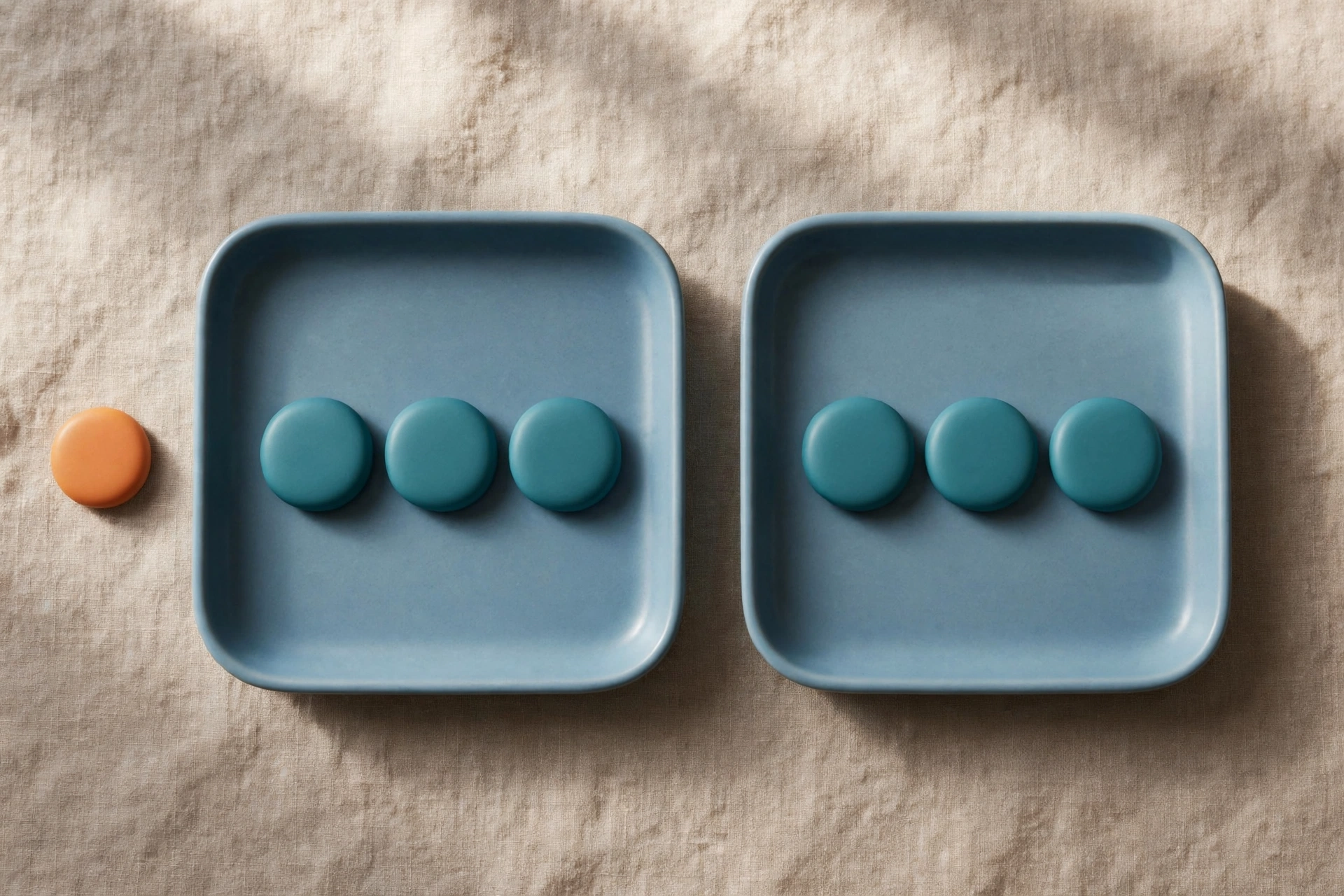 Two blue trays hold teal tokens, with an orange token placed beside one tray on a textured surface.