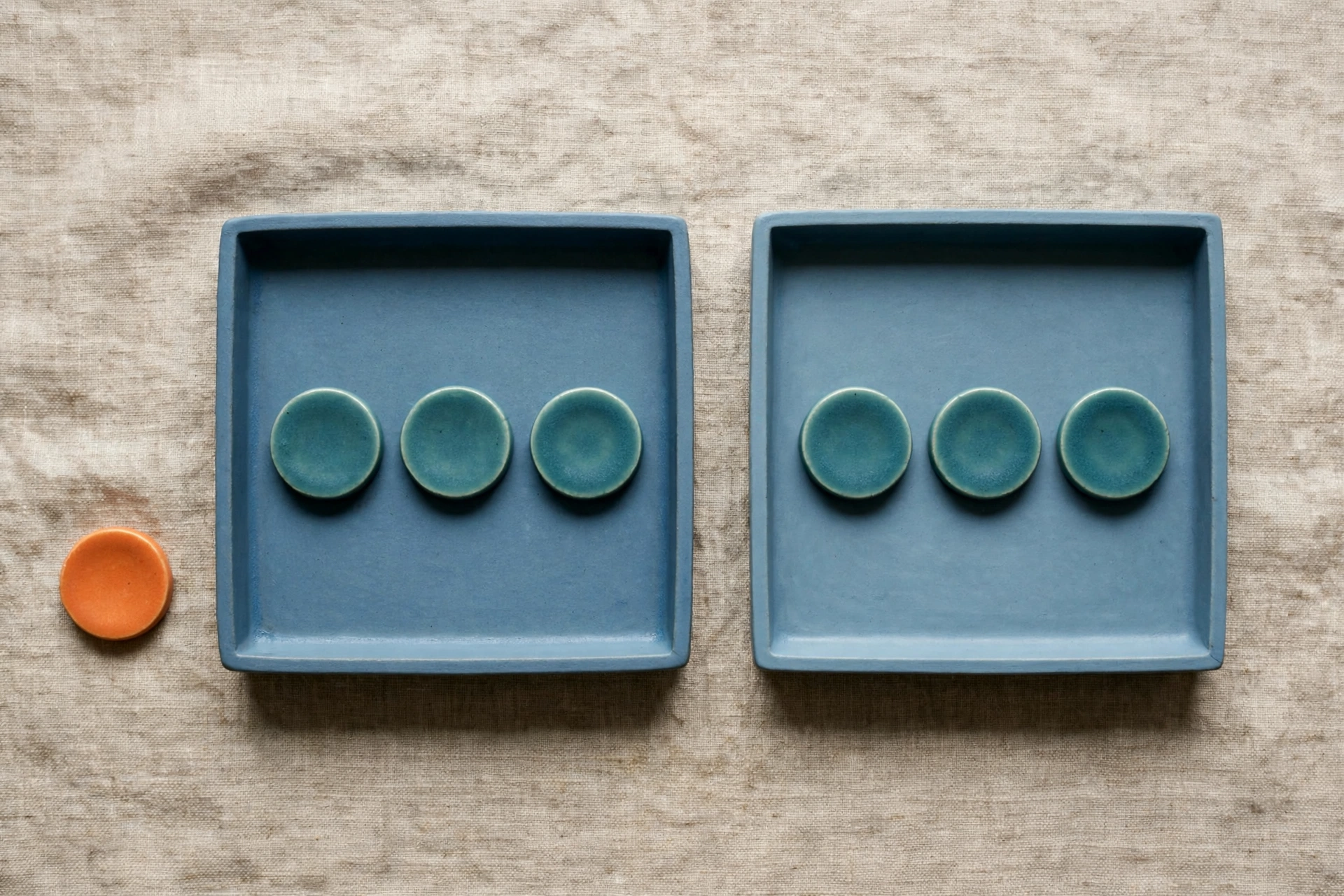 Two blue trays with teal tokens and an orange token outside rest on a textured surface.