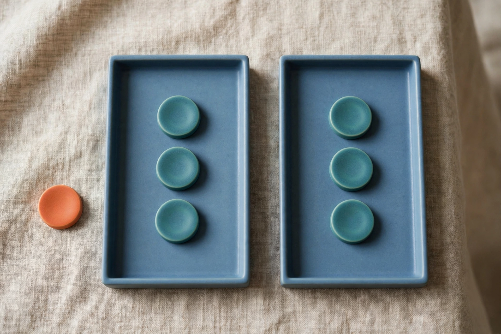 Two blue trays each hold three teal tokens, with a single orange token placed beside the left tray.
