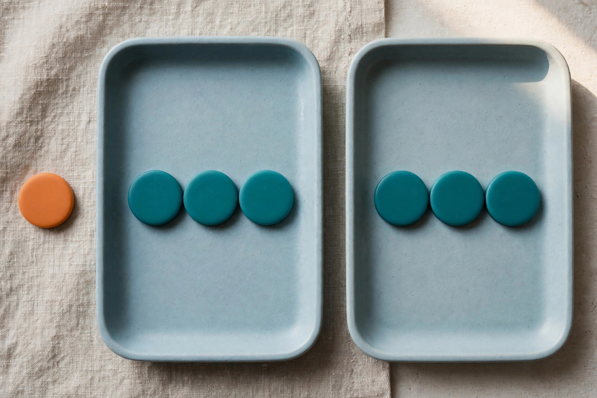 Two blue trays hold teal tokens, with an orange token placed beside one tray on a textured surface.