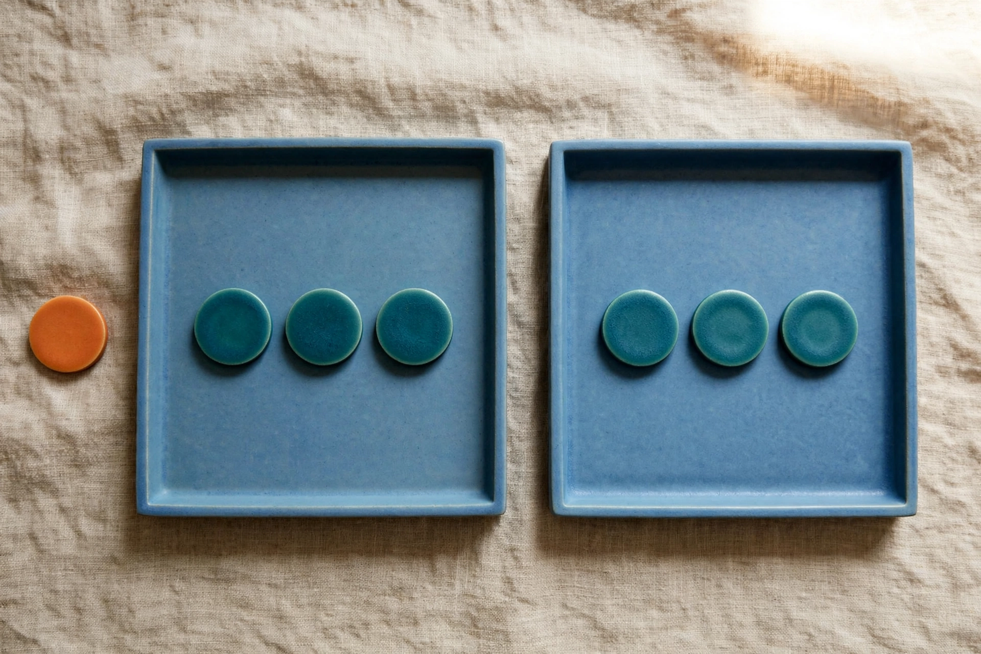 Two blue trays with teal tokens and one orange token outside the left tray on a textured surface.