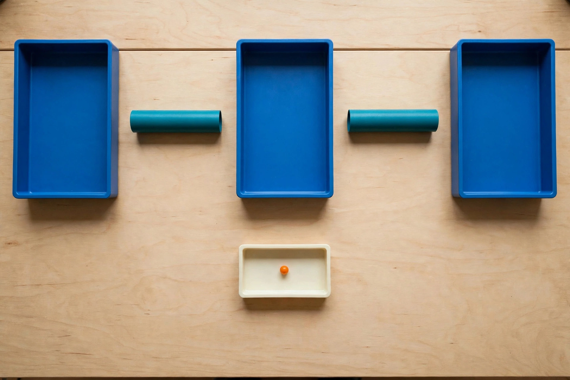 Three blue trays and two teal cylinders are arranged on a wooden surface, with a small orange bead in a lower ivory tray.