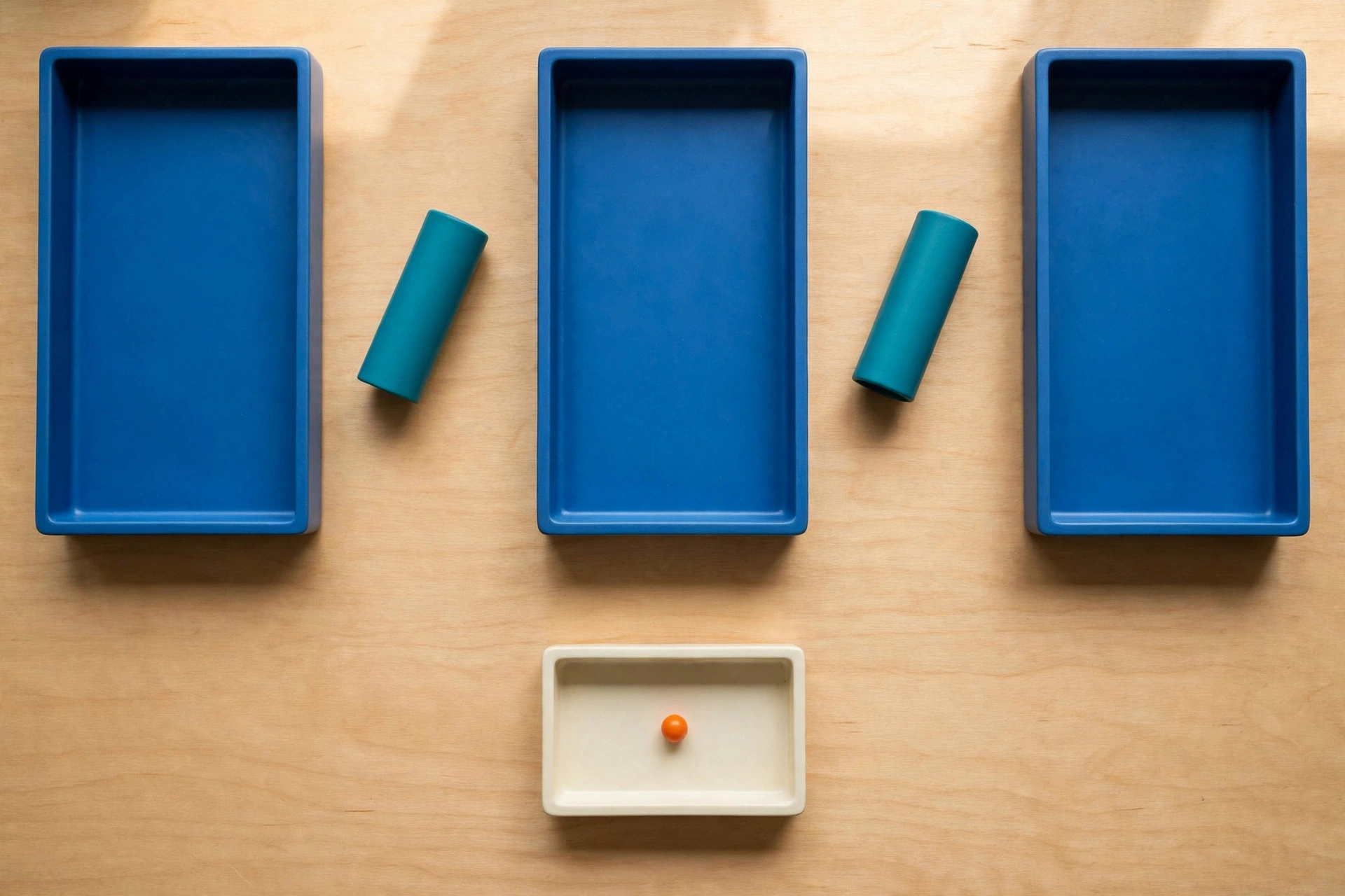 Three blue rectangular trays are arranged in a row on a wooden surface, with teal cylinders placed in the gaps between them.