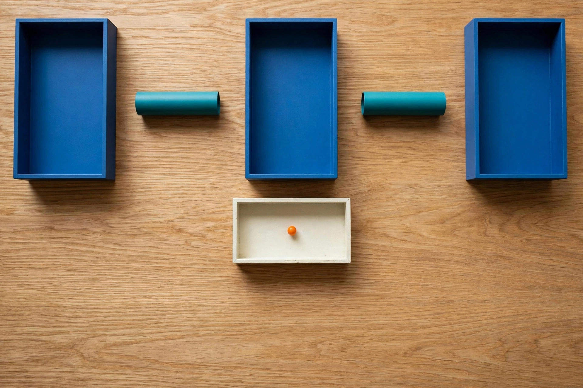 Three blue rectangular trays are arranged in a row on a wooden surface, with teal cylinders placed in the gaps between them.