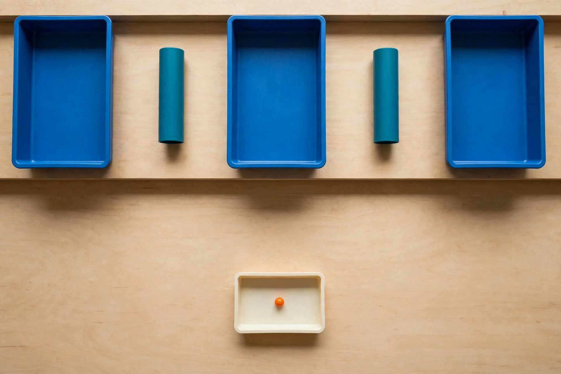 Three blue rectangular trays and two teal cylinders are arranged on a wooden surface, with a smaller ivory tray containing an orange bead below.