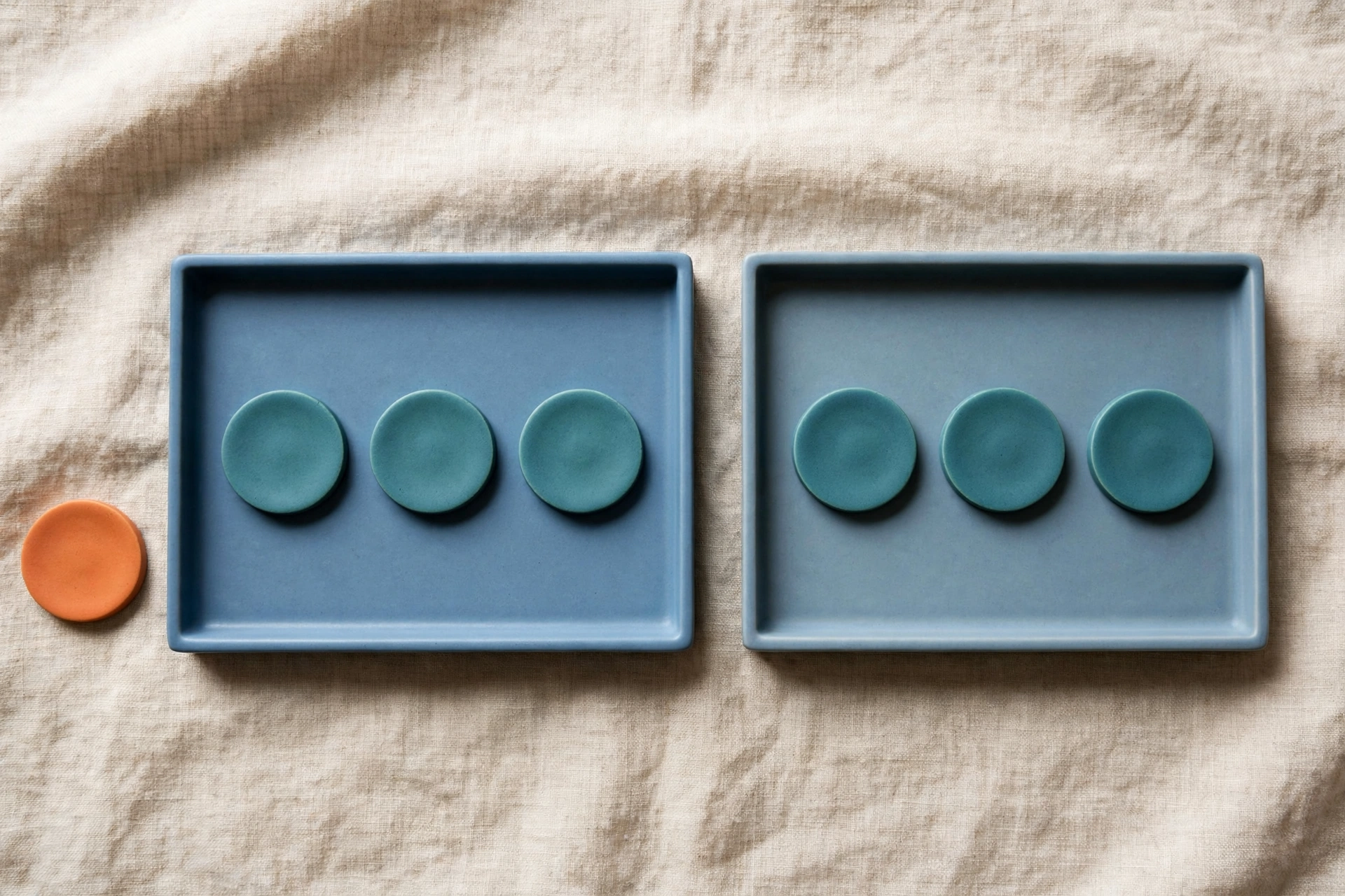 Two blue trays each hold three teal tokens, with a single orange token placed beside the left tray on a textured cloth.