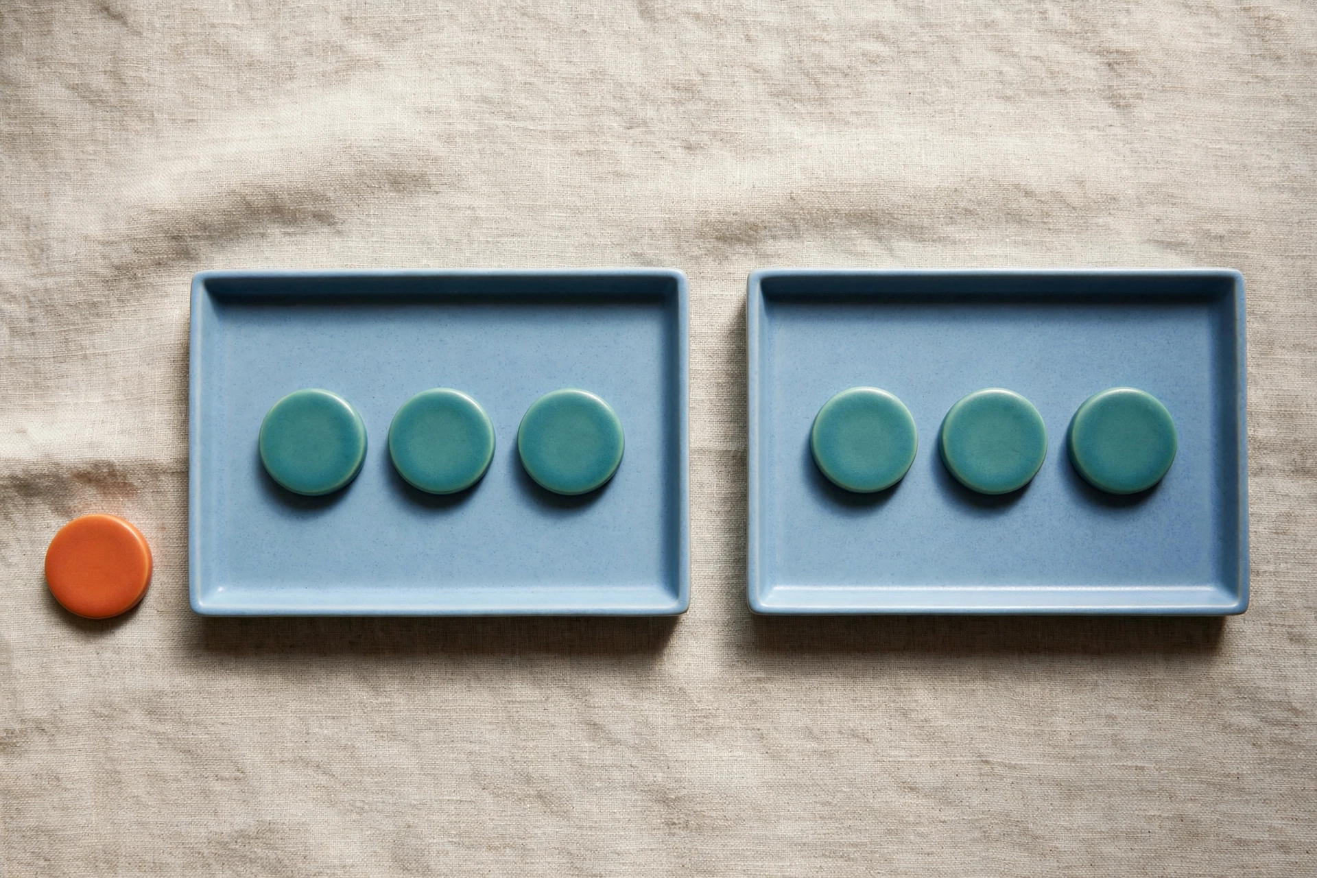Two blue trays each hold three teal tokens, with an orange token placed beside the left tray on a textured surface.