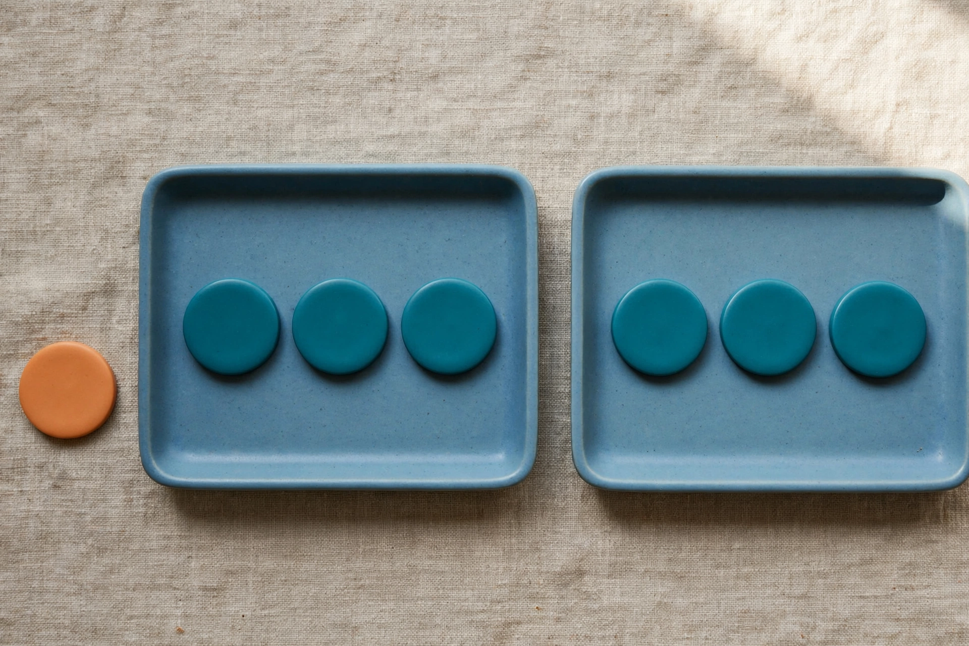 Two blue trays hold teal tokens, with an orange token placed beside one tray on a textured surface.