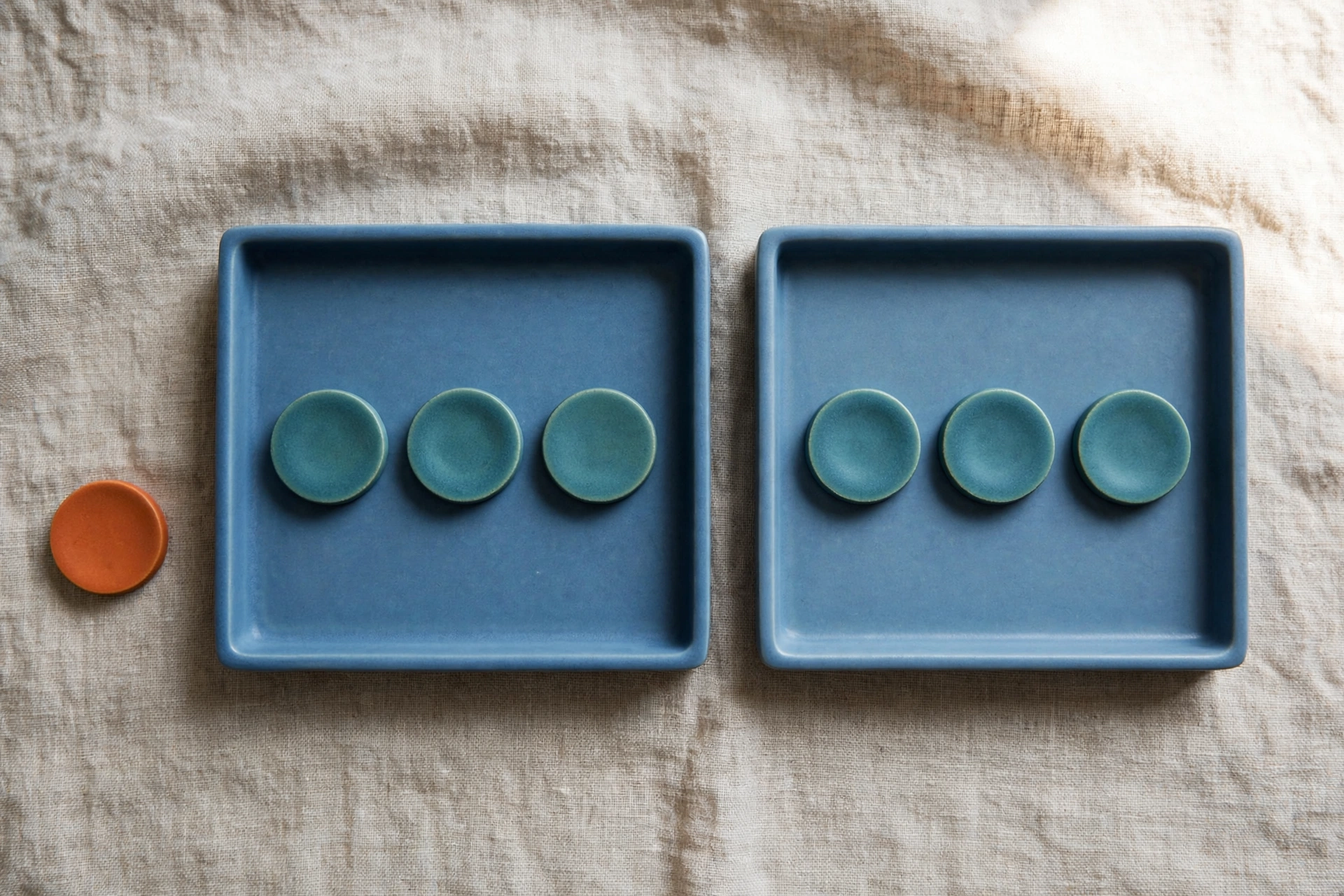 Two blue trays with teal tokens and one orange token beside them on a textured surface.