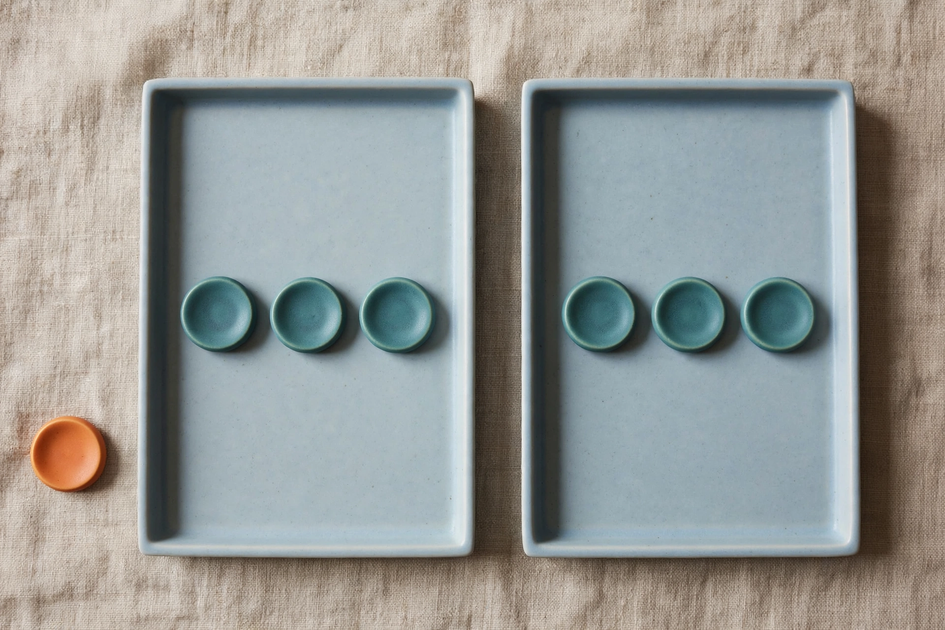 Two shallow blue trays each hold three teal tokens, with a single orange token placed beside the left tray.