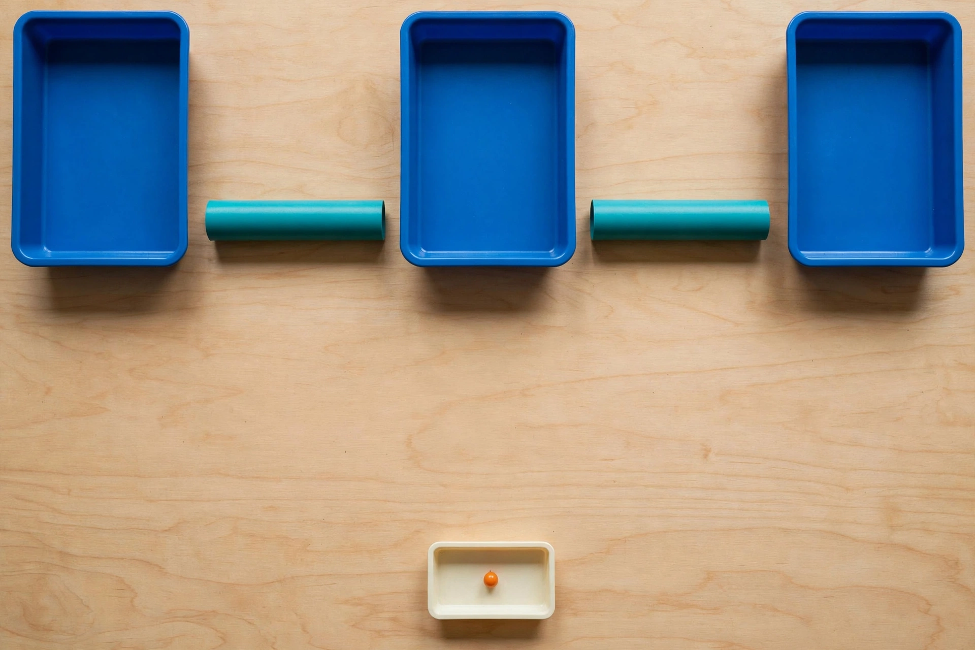 Three blue trays and two teal cylinders are arranged on a wooden surface, with a small ivory tray containing an orange bead below.