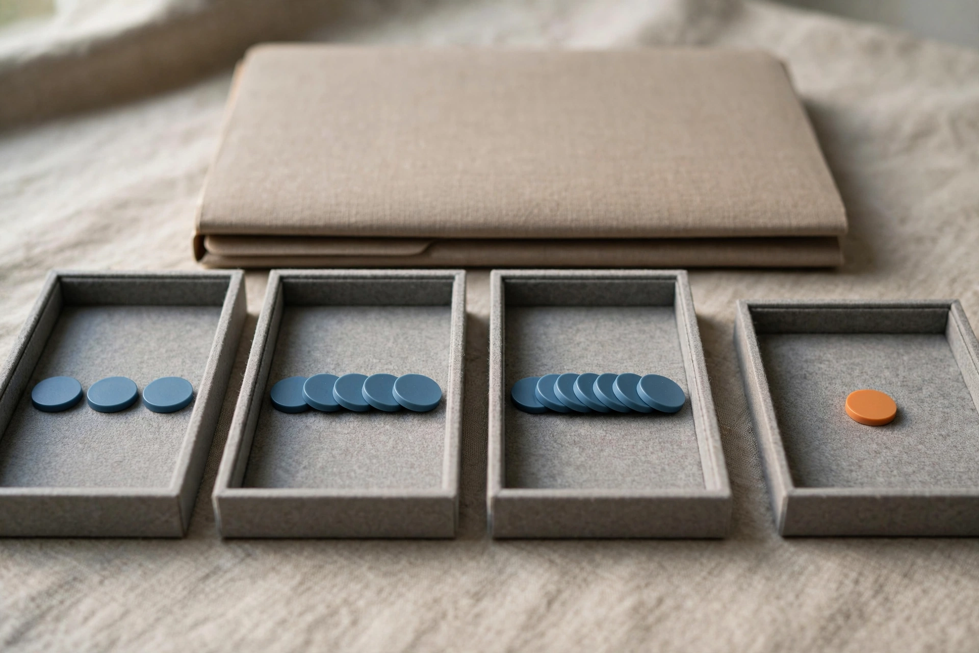 Four gray trays with blue tokens progress from left to right, with a single orange token in the rightmost tray, behind a closed folder.
