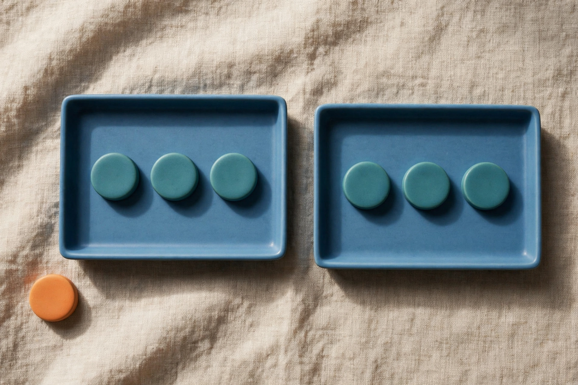 Two blue trays each hold three teal tokens, with a single orange token placed beside the left tray.