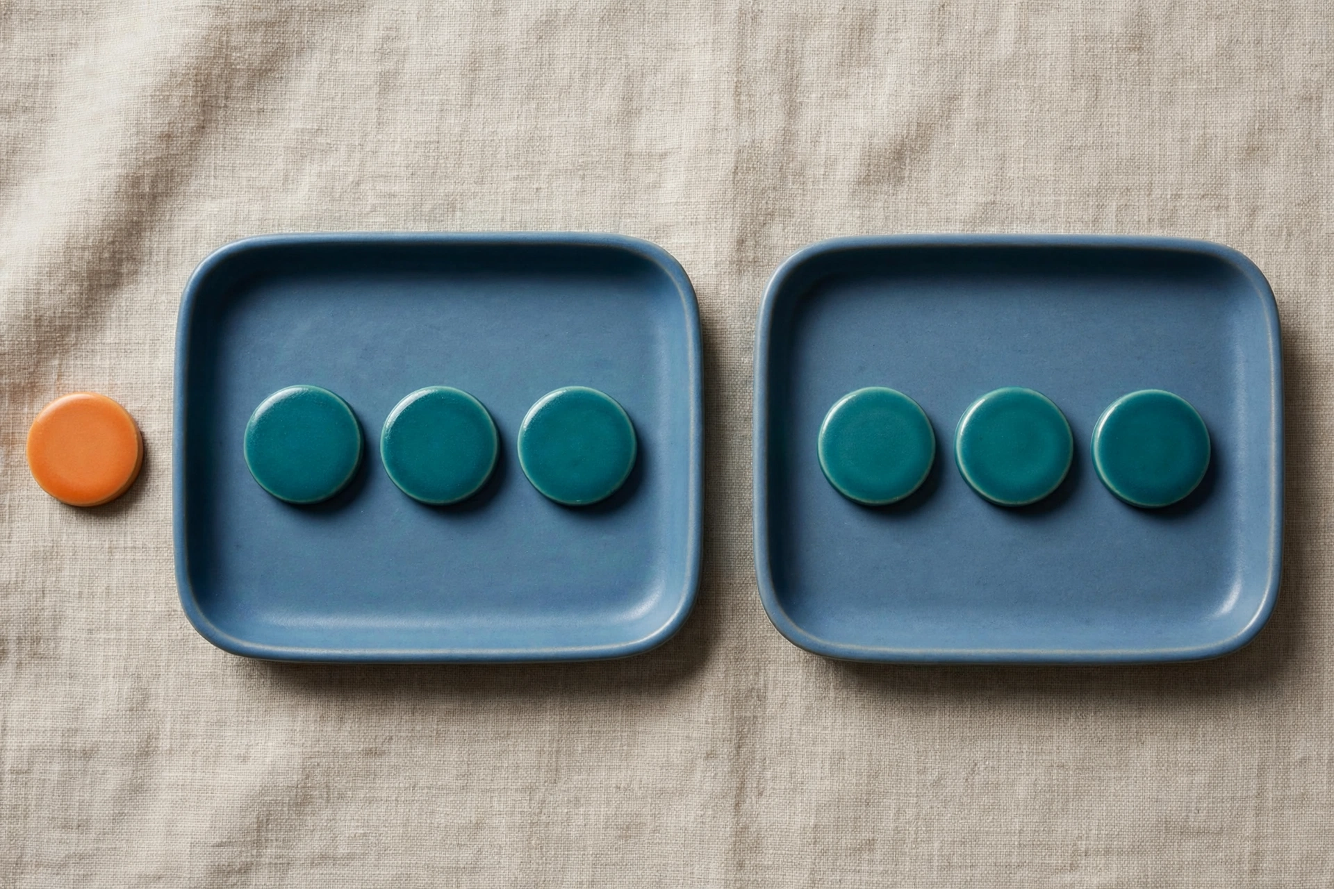 Two blue trays each hold three teal tokens, with one orange token placed beside the left tray on a textured surface.