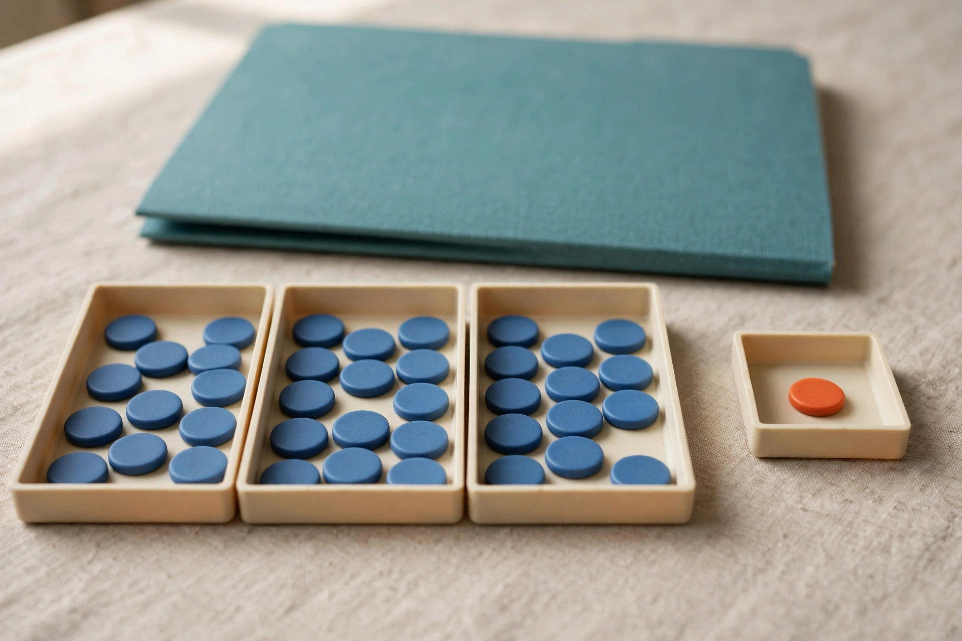 Blue tokens are distributed in three trays, with one orange token in a separate small tray, and a teal folder behind.