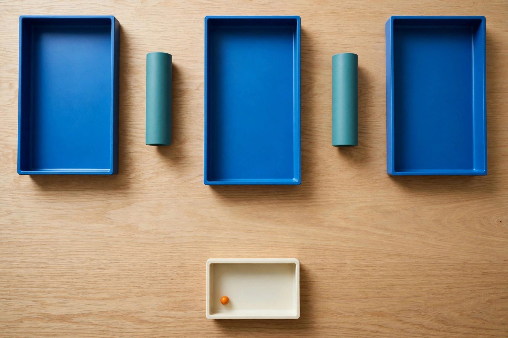 Three blue rectangular trays are arranged in a row on a wooden surface, with teal cylinders placed in the gaps between them.