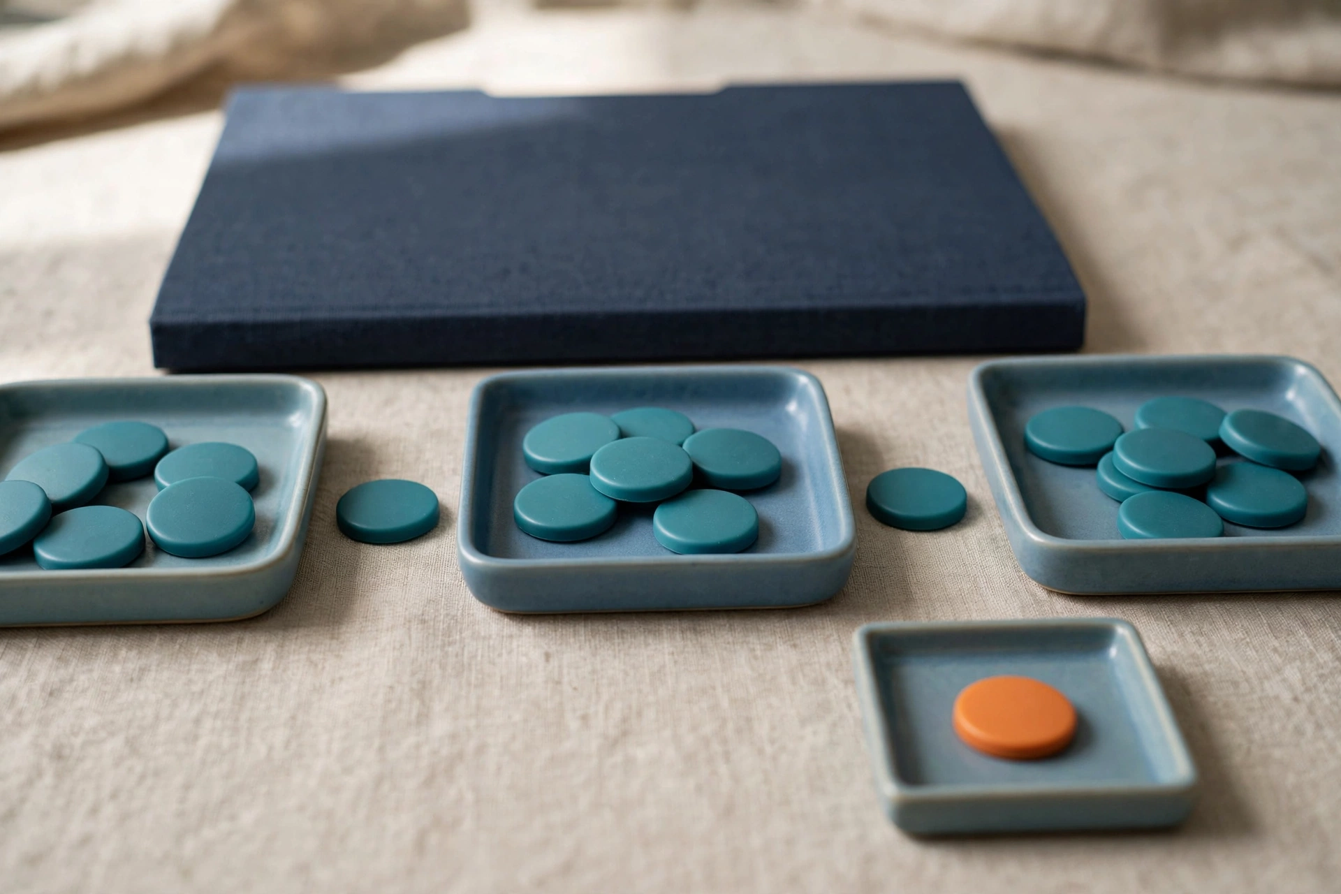 Three blue trays with teal tokens are arranged in a sequence, with a separate tray holding an orange token, and a closed blue folder behind.