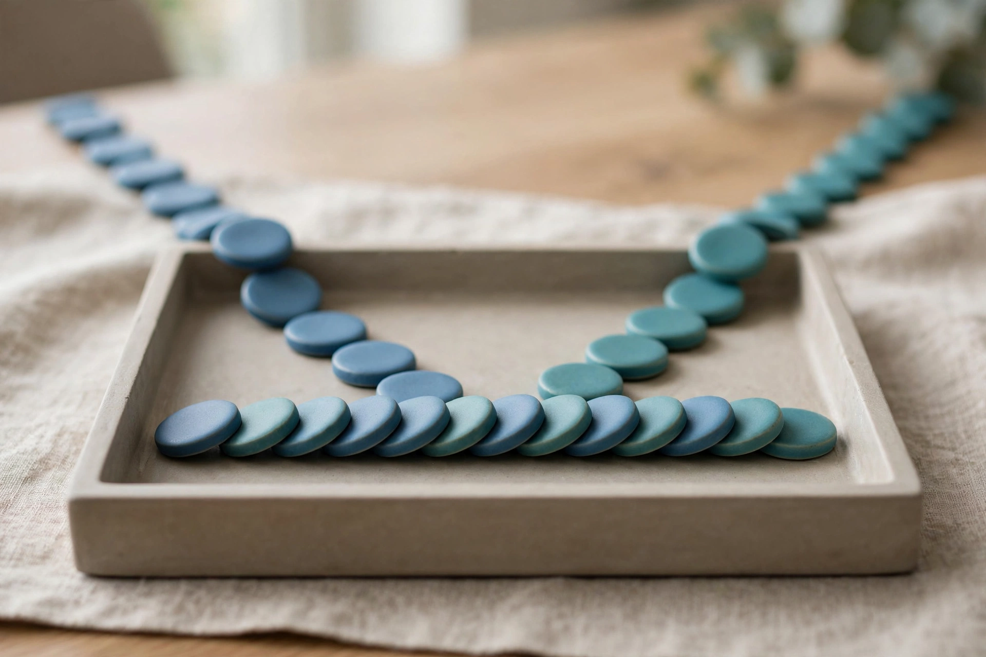Two streams of blue and teal ceramic tokens converge into a single ordered row within a shallow sorting tray.