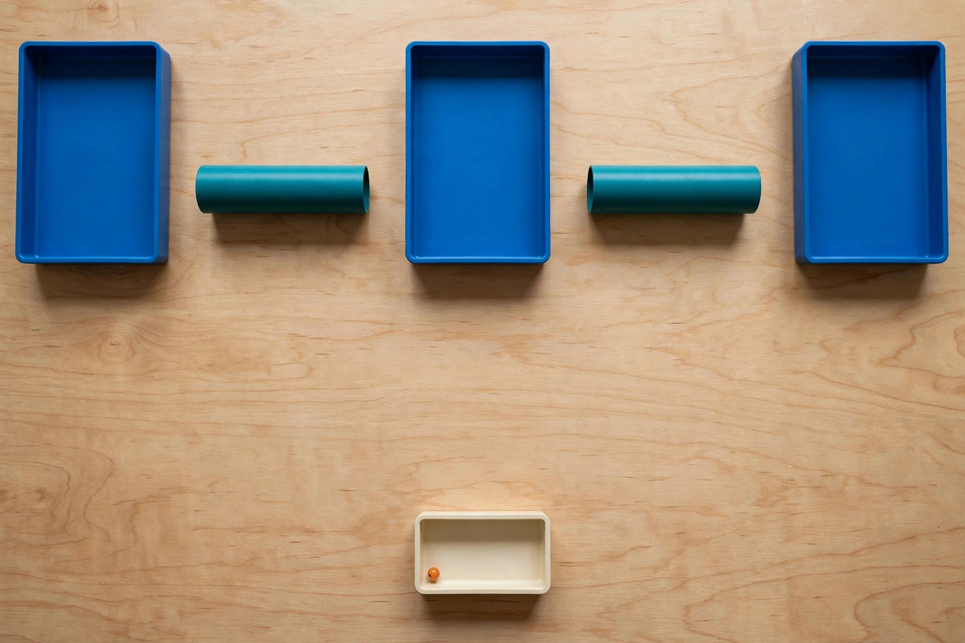 Three blue trays are arranged in a row with teal cylinders in the gaps between them, and a small ivory tray with an orange bead sits below.