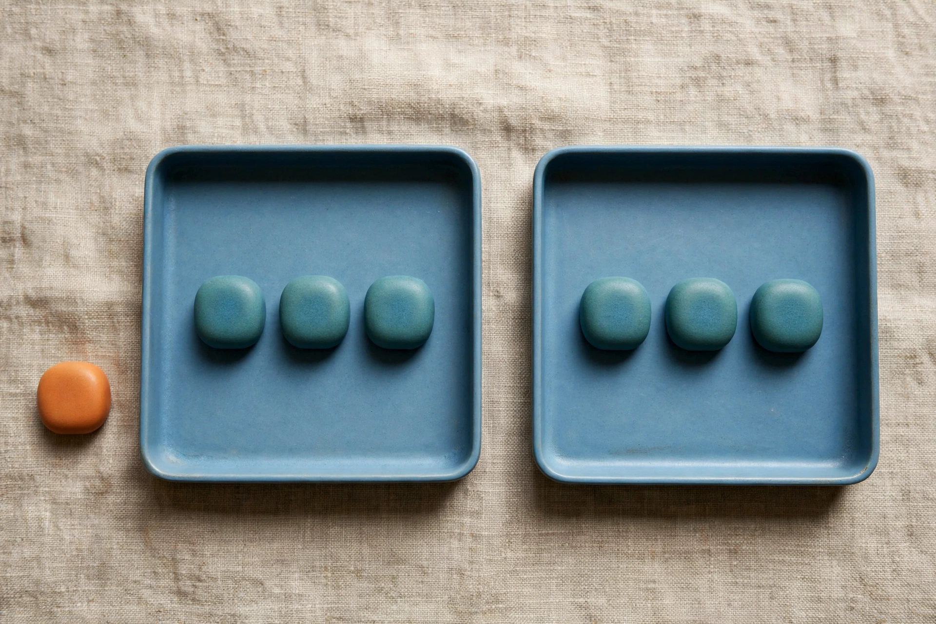 Two blue trays each hold three teal tokens, with one orange token placed beside the left tray on a textured surface.