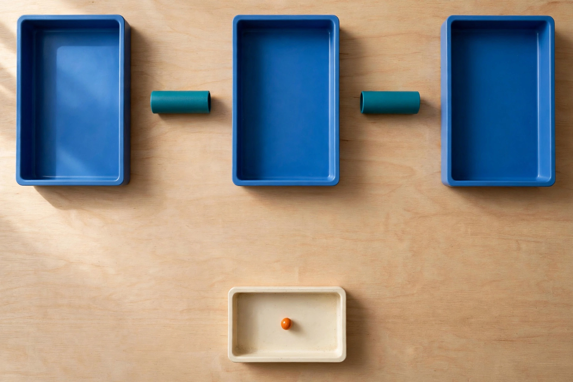 Three blue rectangular trays are arranged horizontally on a wooden surface, with teal cylinders in the gaps between them.