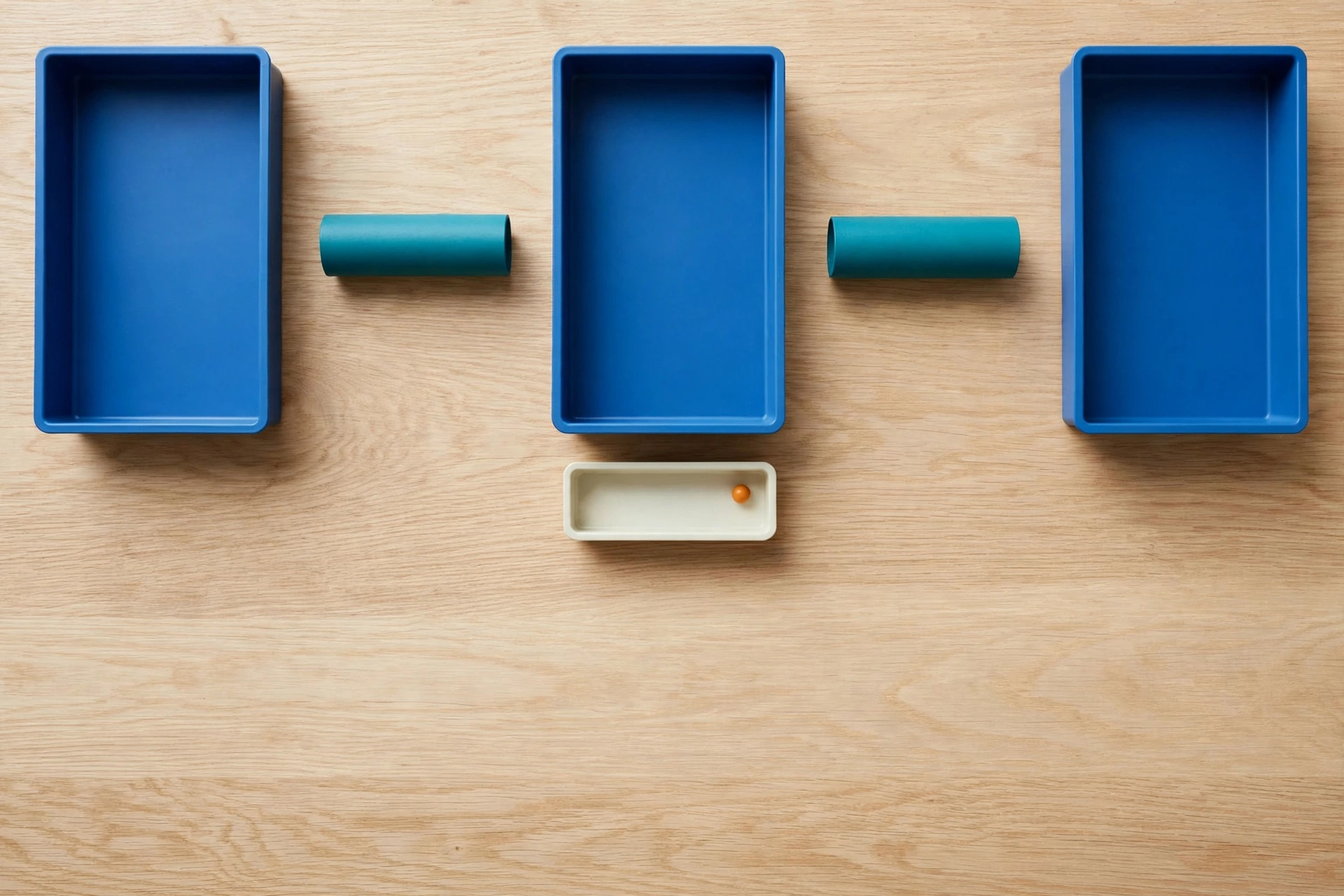 Three blue trays and two teal cylinders are arranged on a wooden surface, with an ivory tray containing an orange bead below.