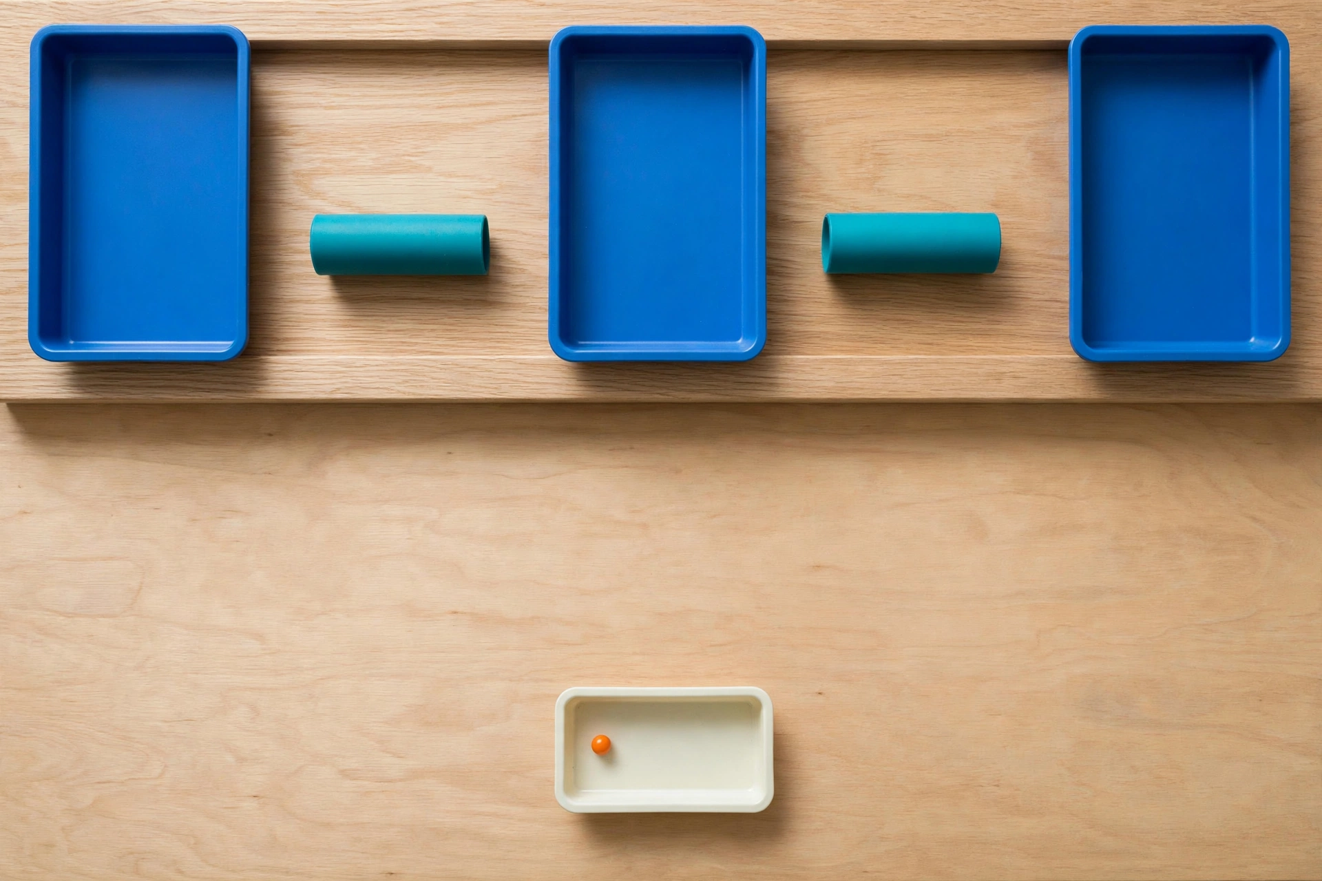 Three blue trays and two teal cylinders are arranged on a wooden surface, with a smaller ivory tray holding an orange bead below.