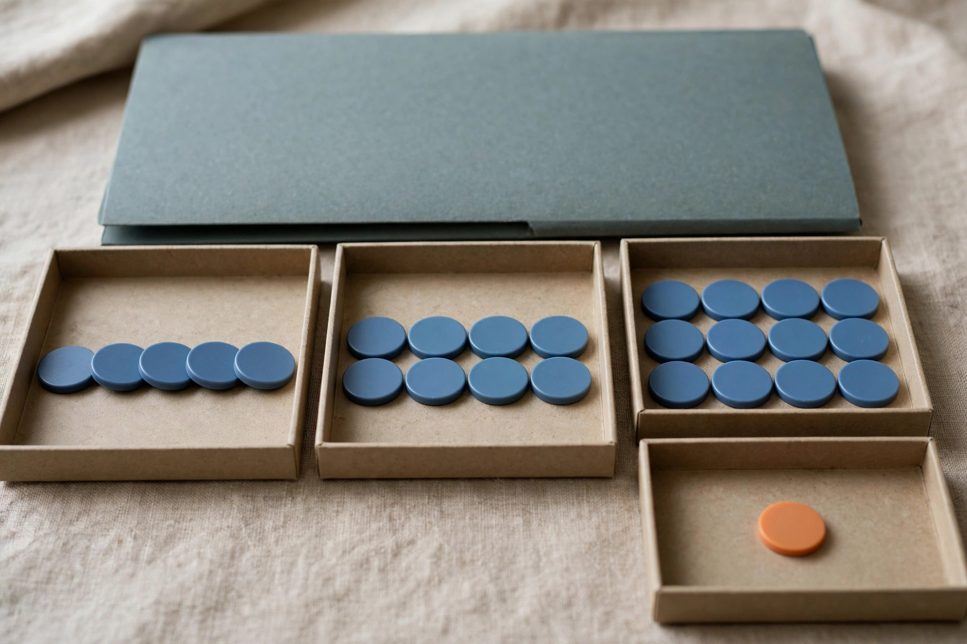 Three shallow office trays with blue tokens progress from left to right, with a fourth tray holding a single orange token to the right.