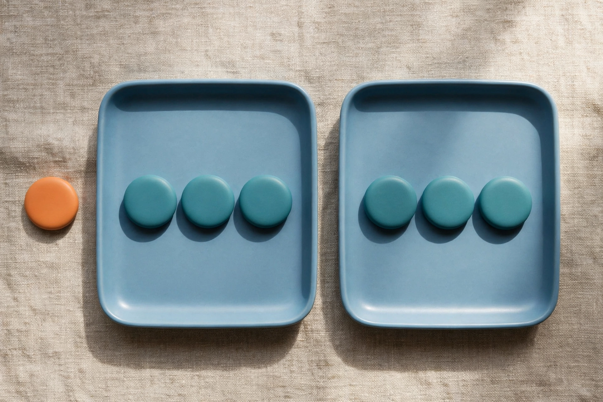 Two blue trays with teal tokens sit side-by-side on a textured surface, with an orange token placed to the left of the left tray.