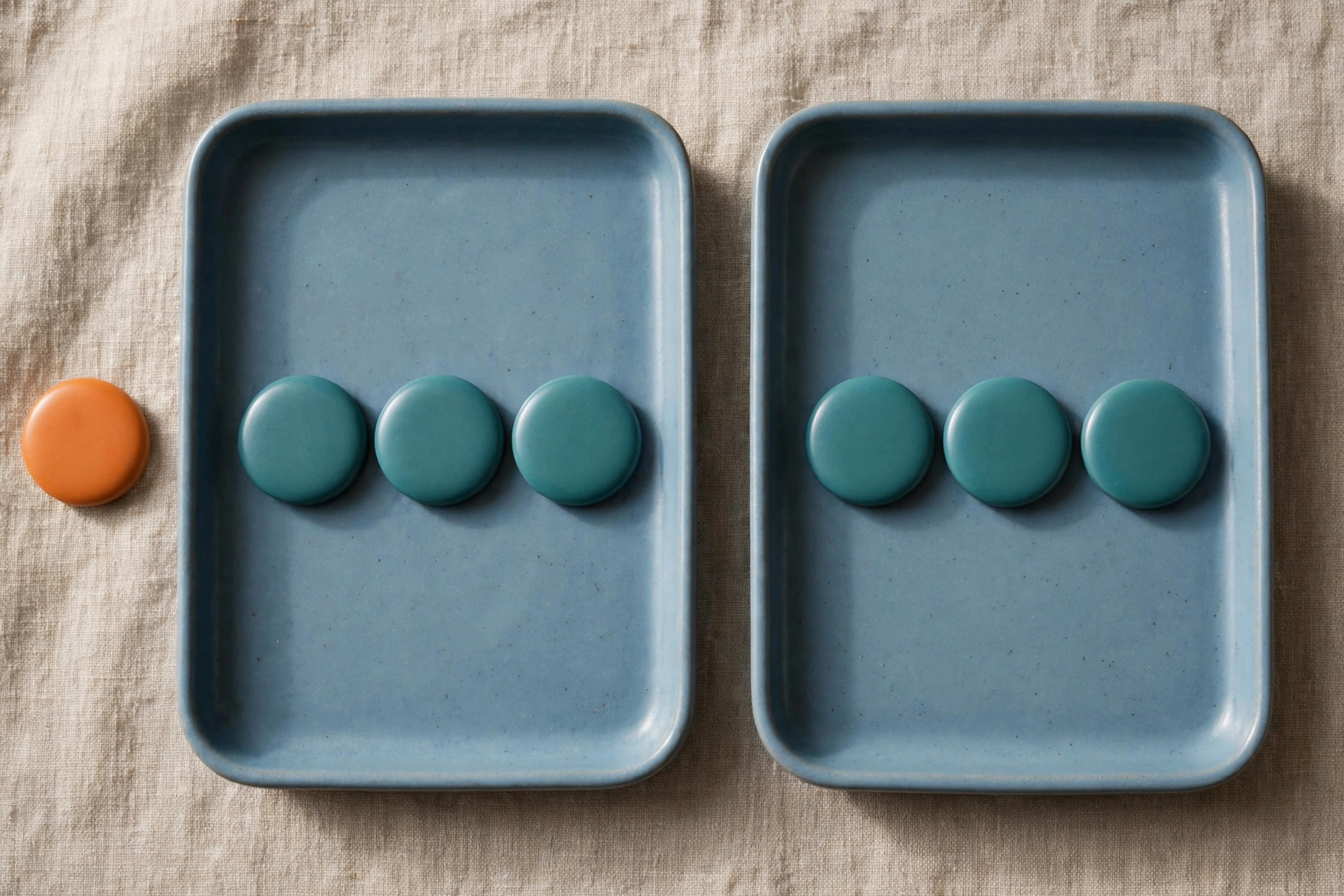 Two blue trays hold rows of teal tokens, with an orange token placed beside the left tray on a textured surface.