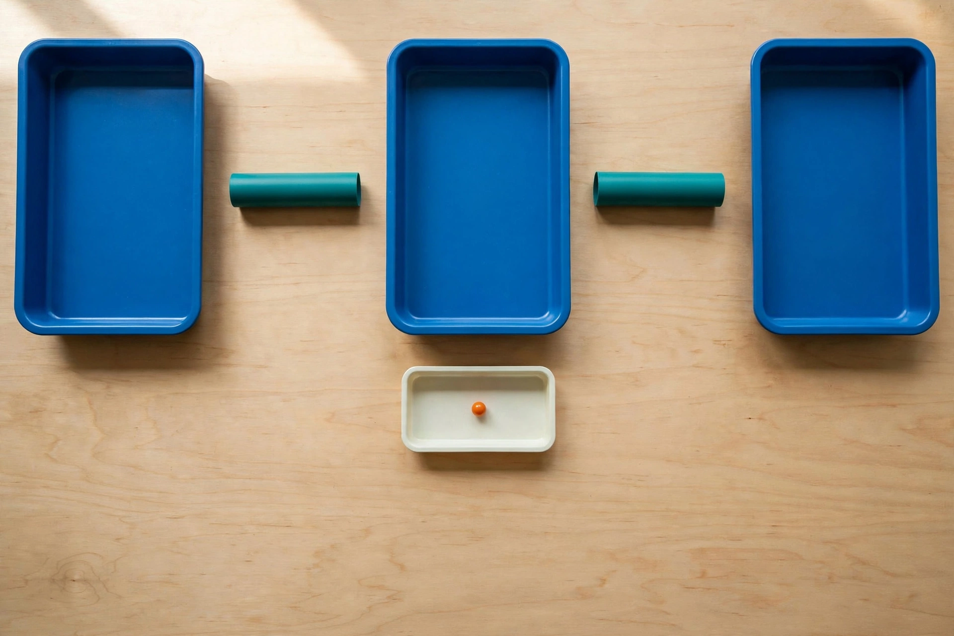 Three blue trays are arranged in a row on a wooden surface, with teal cylinders in the gaps between them.