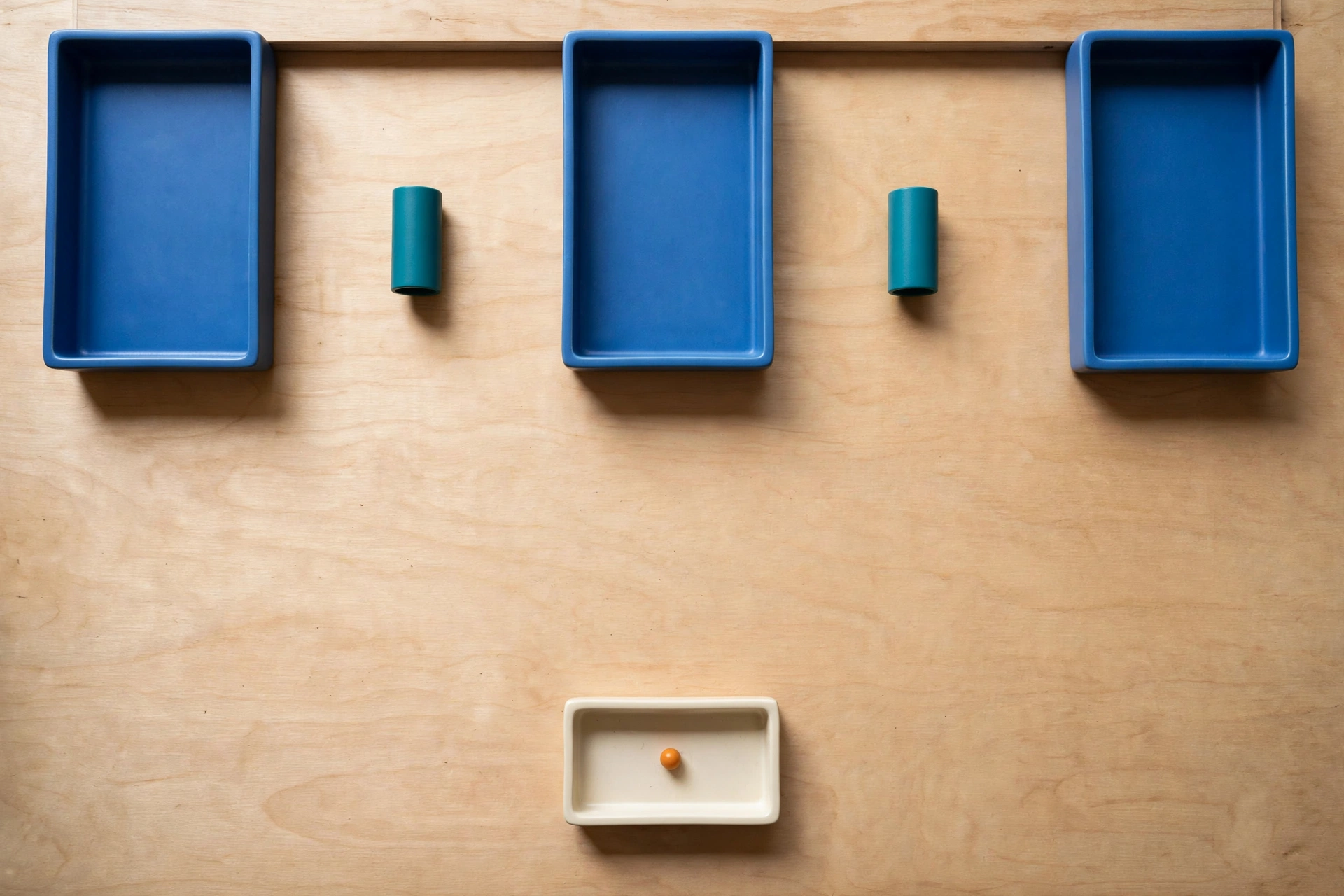 Three blue rectangular trays are arranged in a row above a single ivory rectangular tray containing an orange bead.