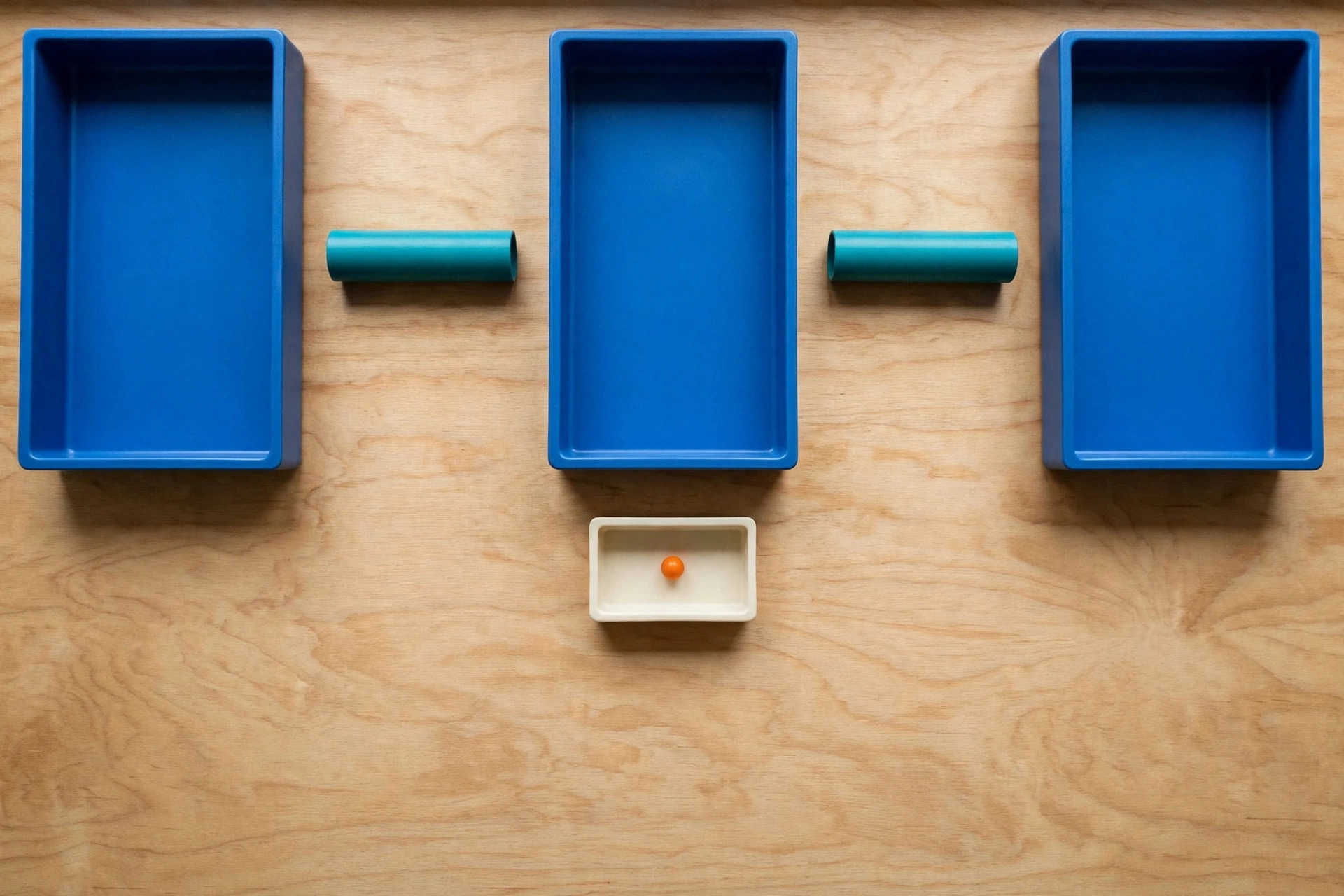 Three blue trays and two teal cylinders are arranged on a wooden surface, with an orange bead in a small ivory tray below.