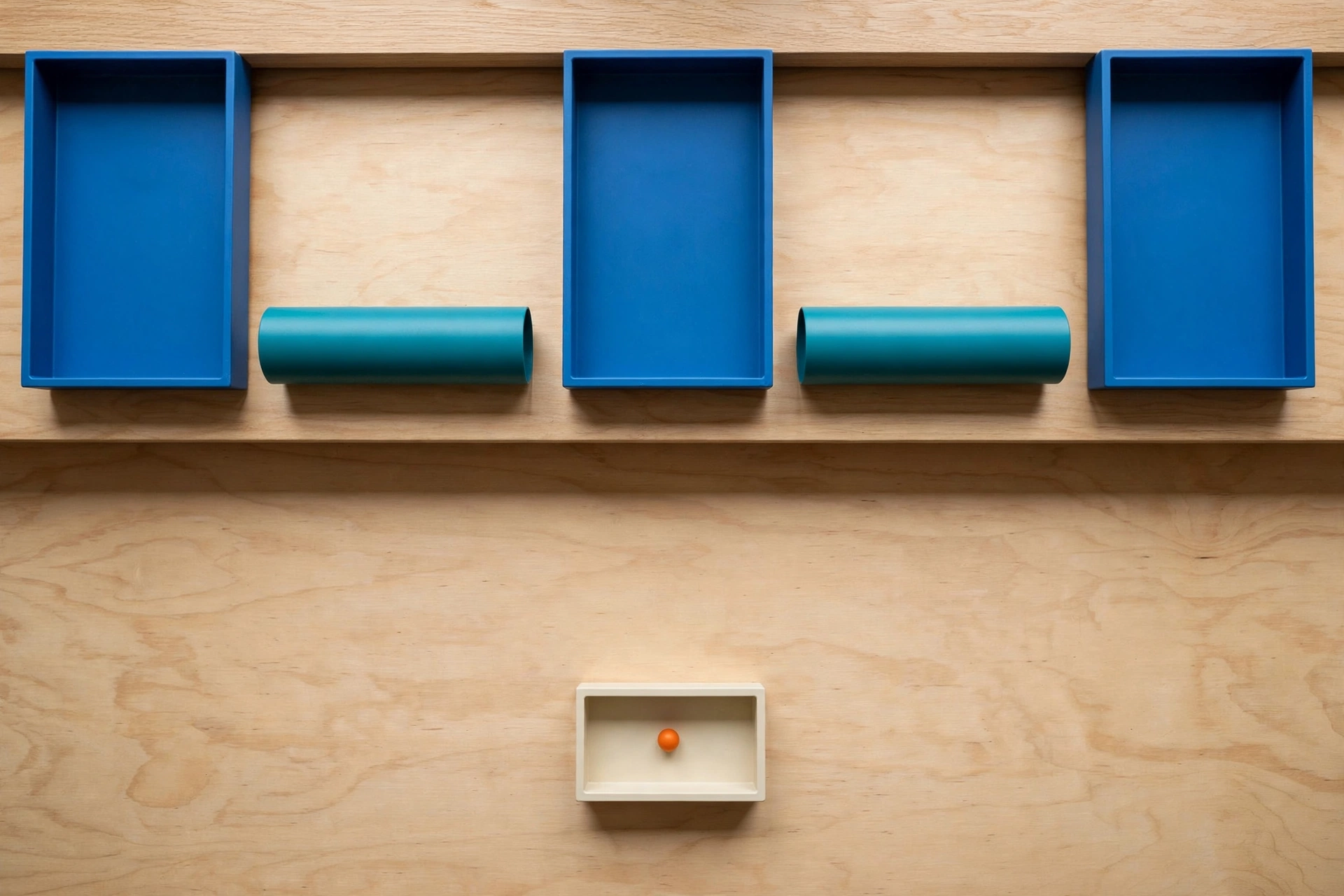 Three blue trays and two teal cylinders are arranged on a wooden surface, with an ivory tray containing an orange bead below.