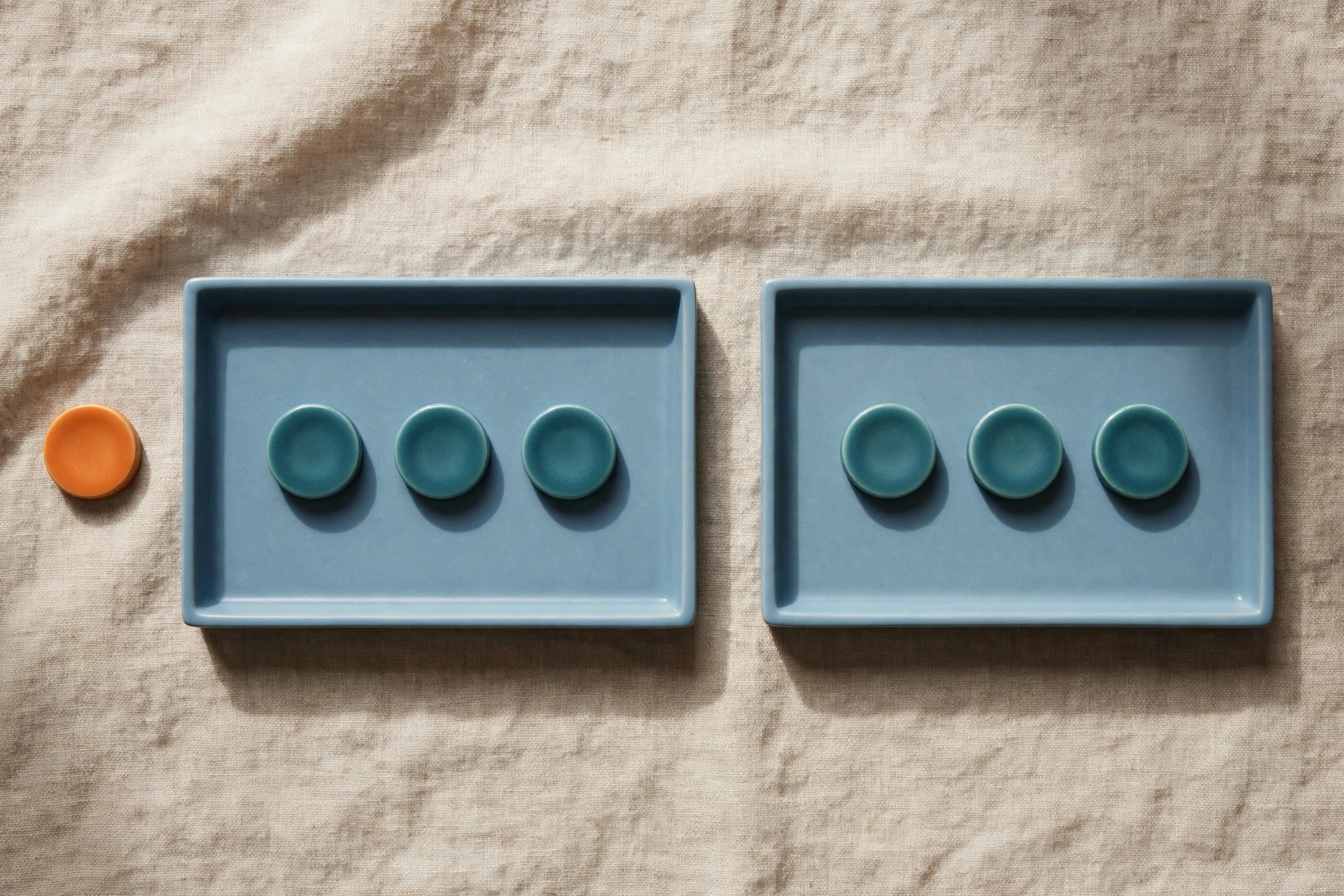 Two blue trays with teal tokens and one orange token beside them on a textured surface.