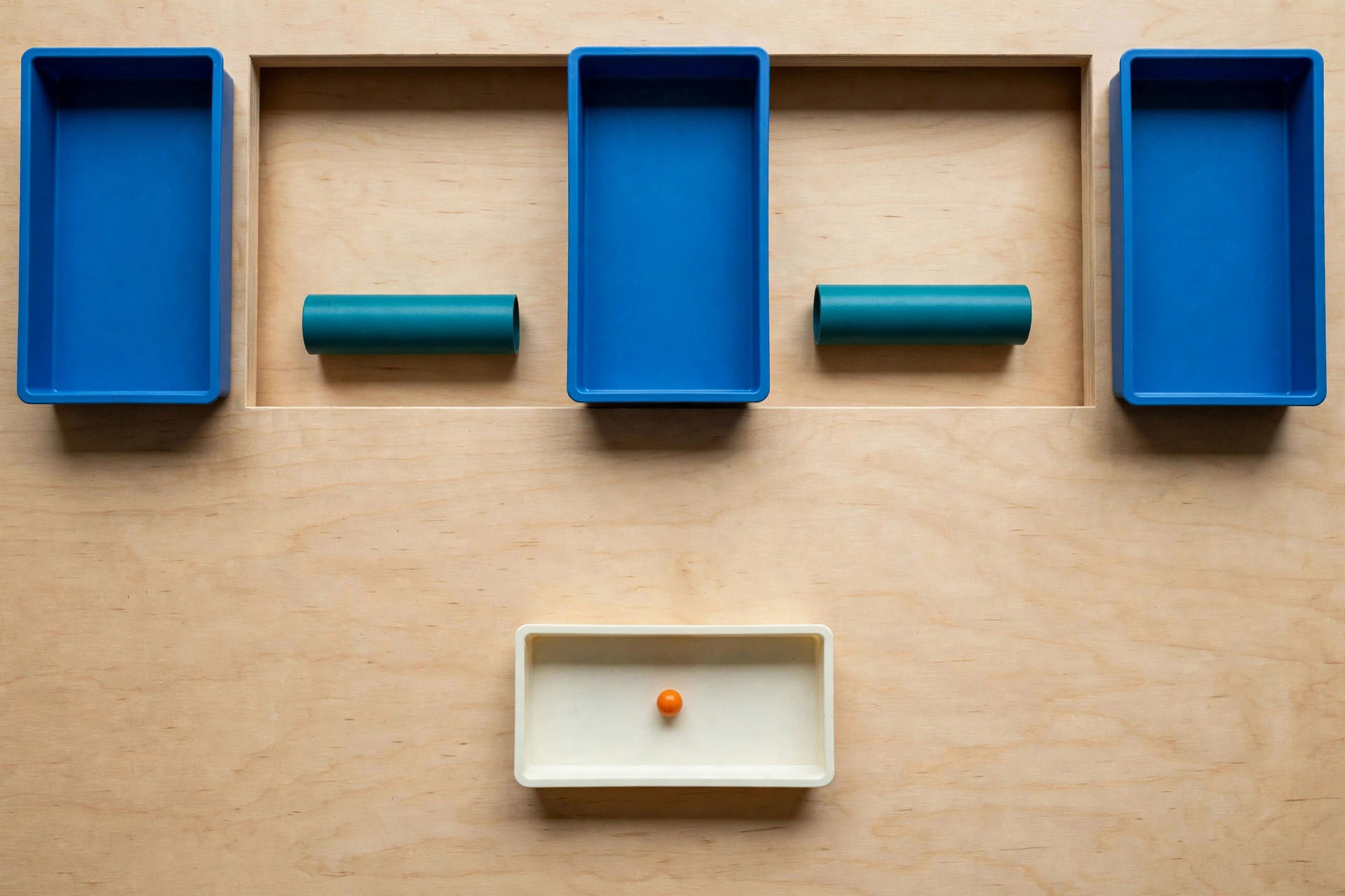 Three blue trays and two teal cylinders are arranged on a wooden surface, with a fourth ivory tray containing an orange bead below.