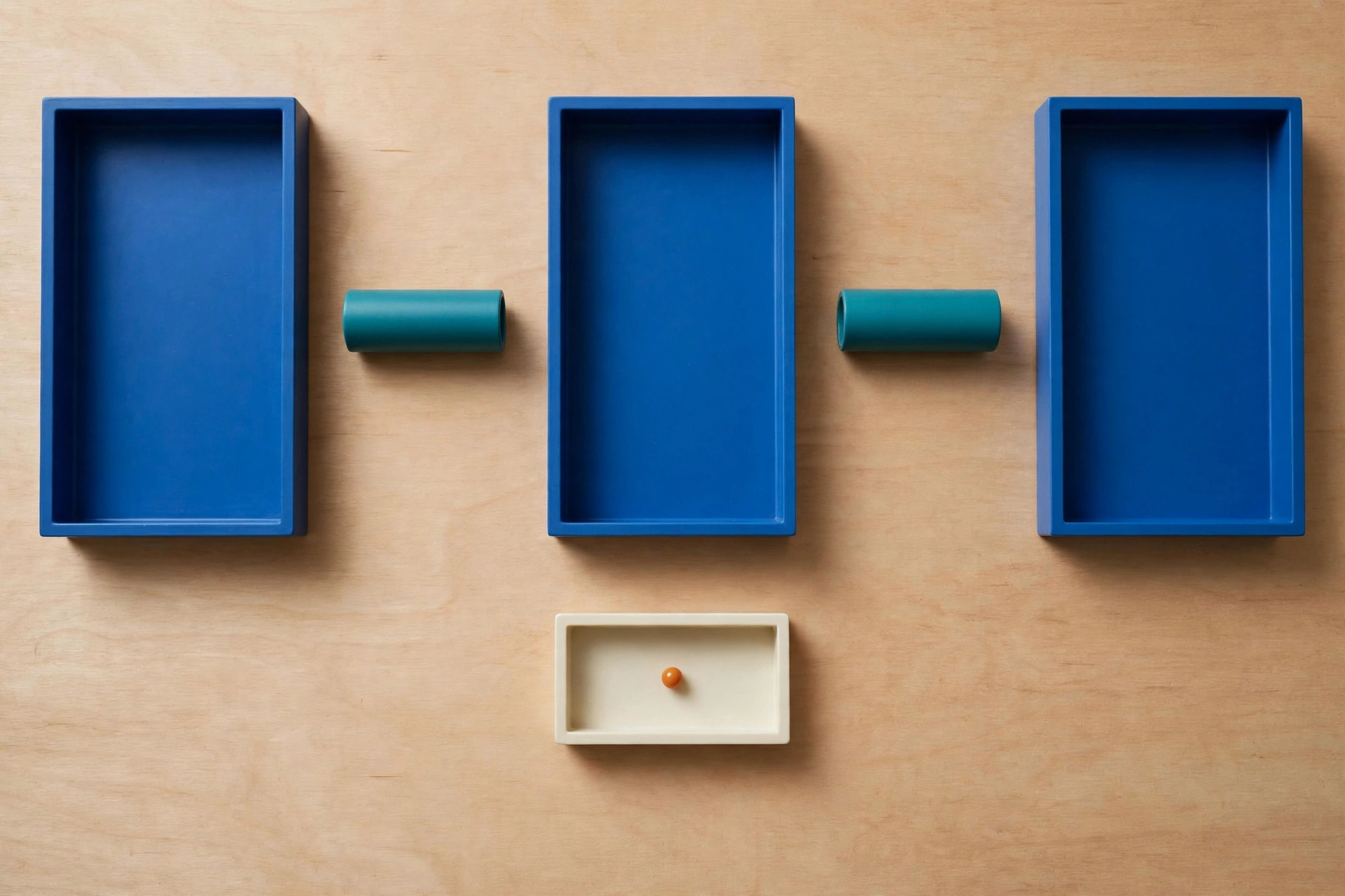 Three blue rectangular trays are arranged in a row with two teal cylinders between them, and a small ivory tray with an orange bead below.